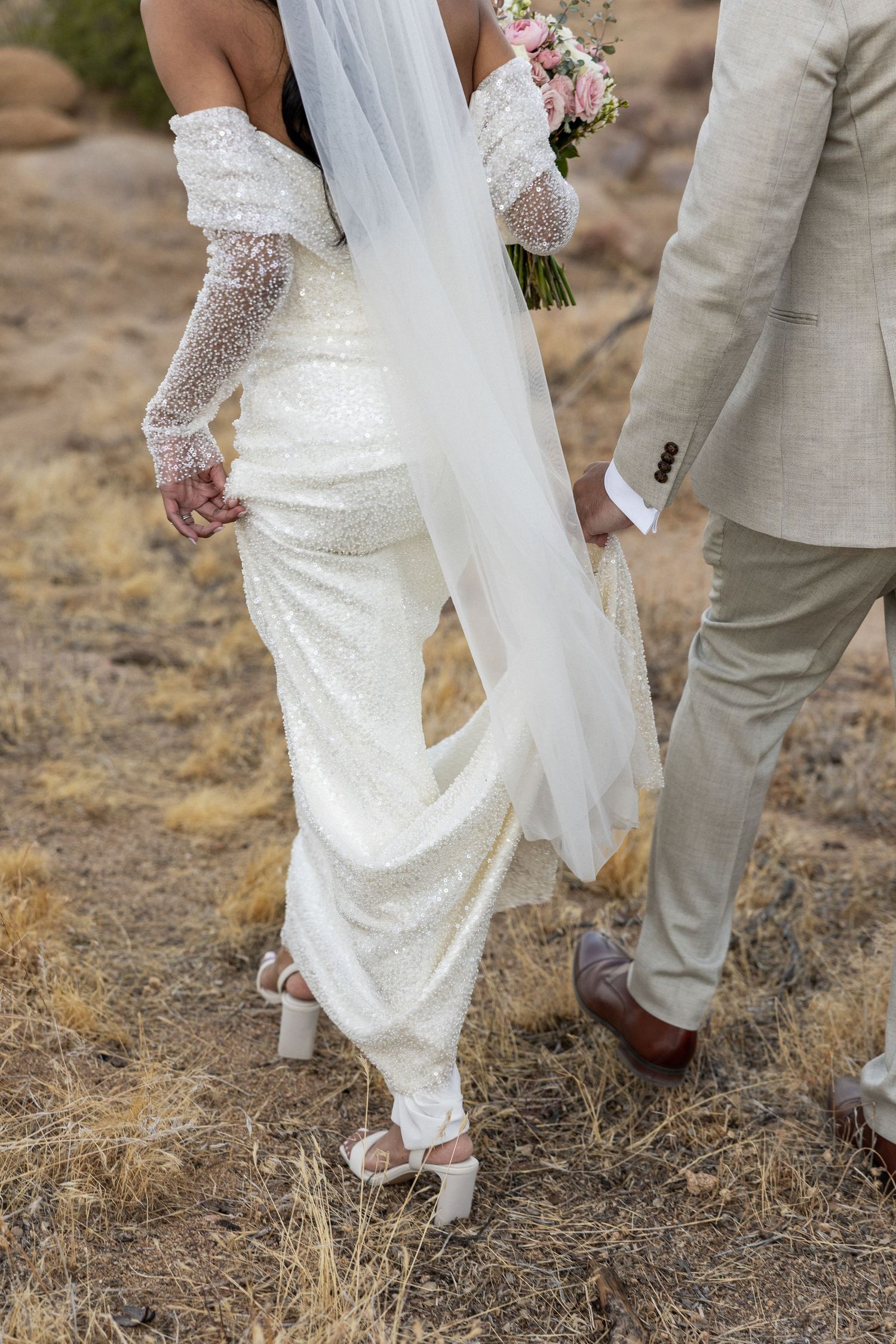 A close-up of a bride in a sequined wedding dress and lace gloves standing next to a groom in a beige suit in Jacksonville North Carolina.