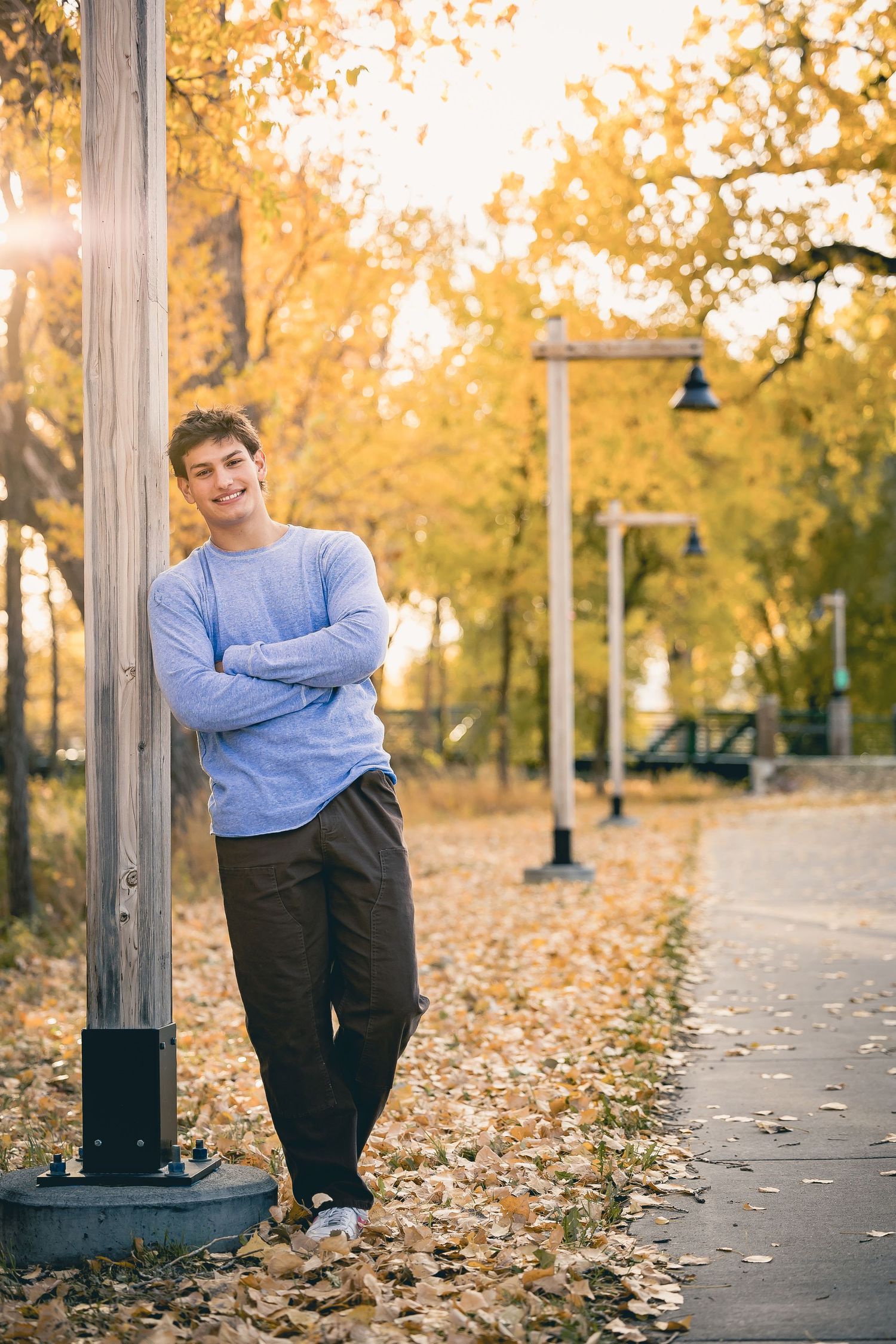 Casual portrait leaning against lamppost with fall foliage in background.