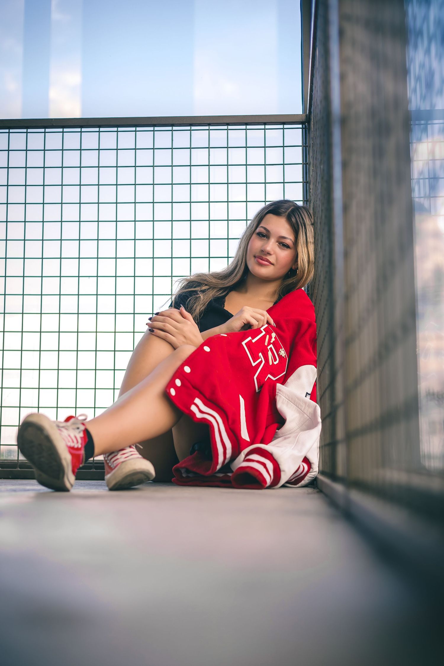 Casual portrait against wire mesh fence wearing red varsity jacket.