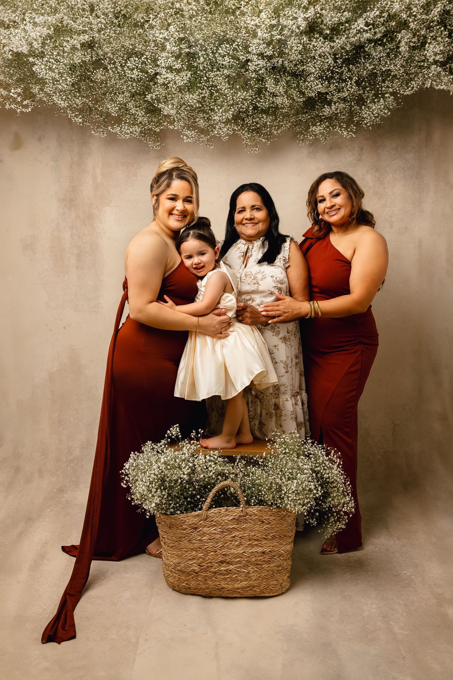 Four people in burgundy and white attire pose in a studio setting with baby's breath flowers and a woven basket decoration.
