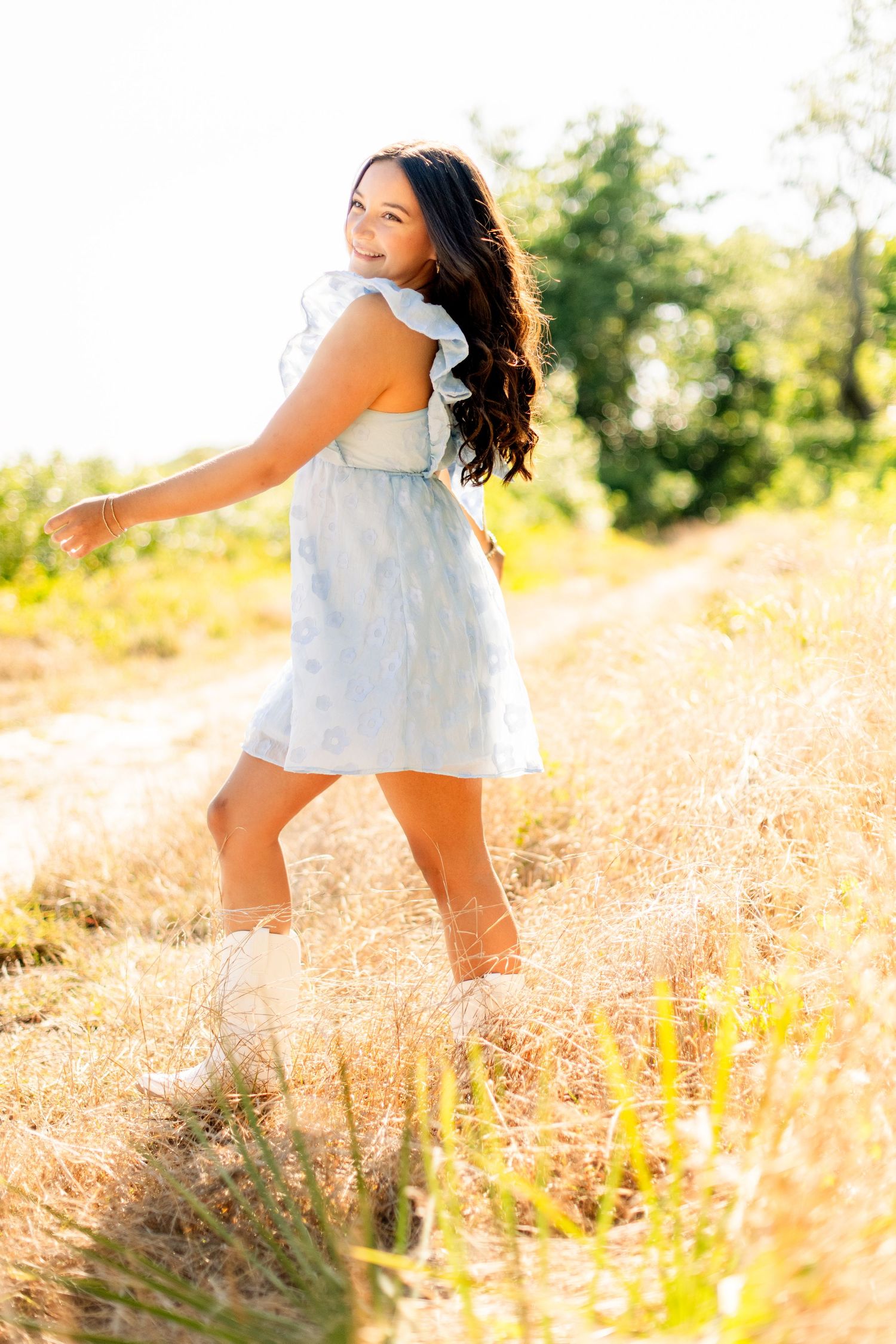A person in a flowing white dress twirls gracefully through a sun-drenched field of golden wildflowers at sunset.