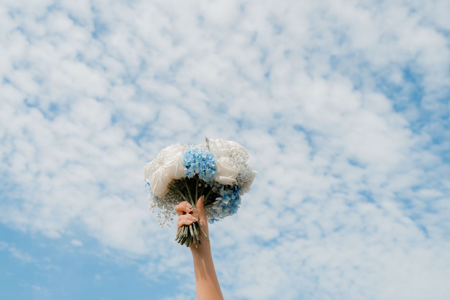 A bouquet held against a bright blue sky with scattered clouds.