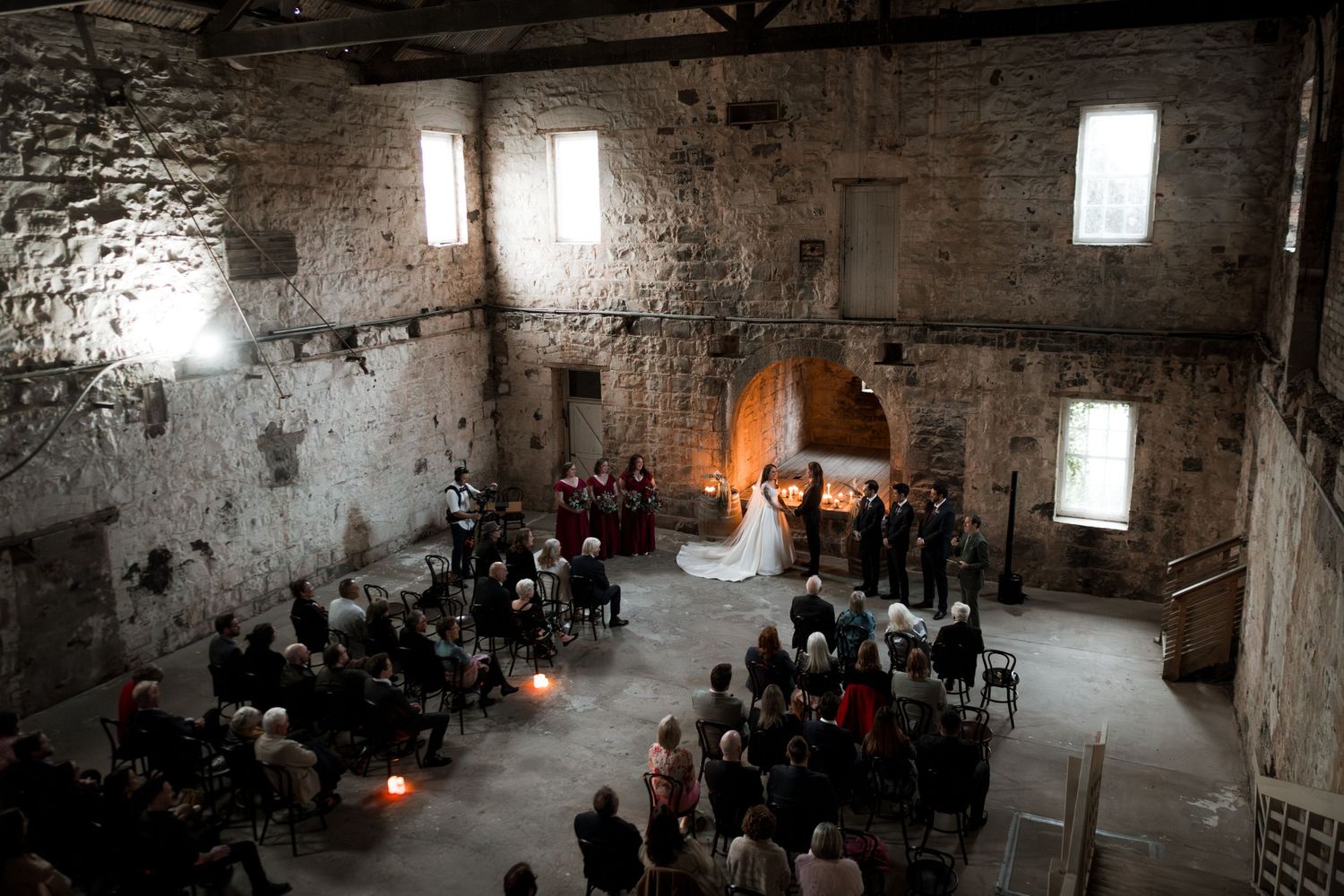 A rustic stone castle interior with candlelit ceremony setup and guests seated.