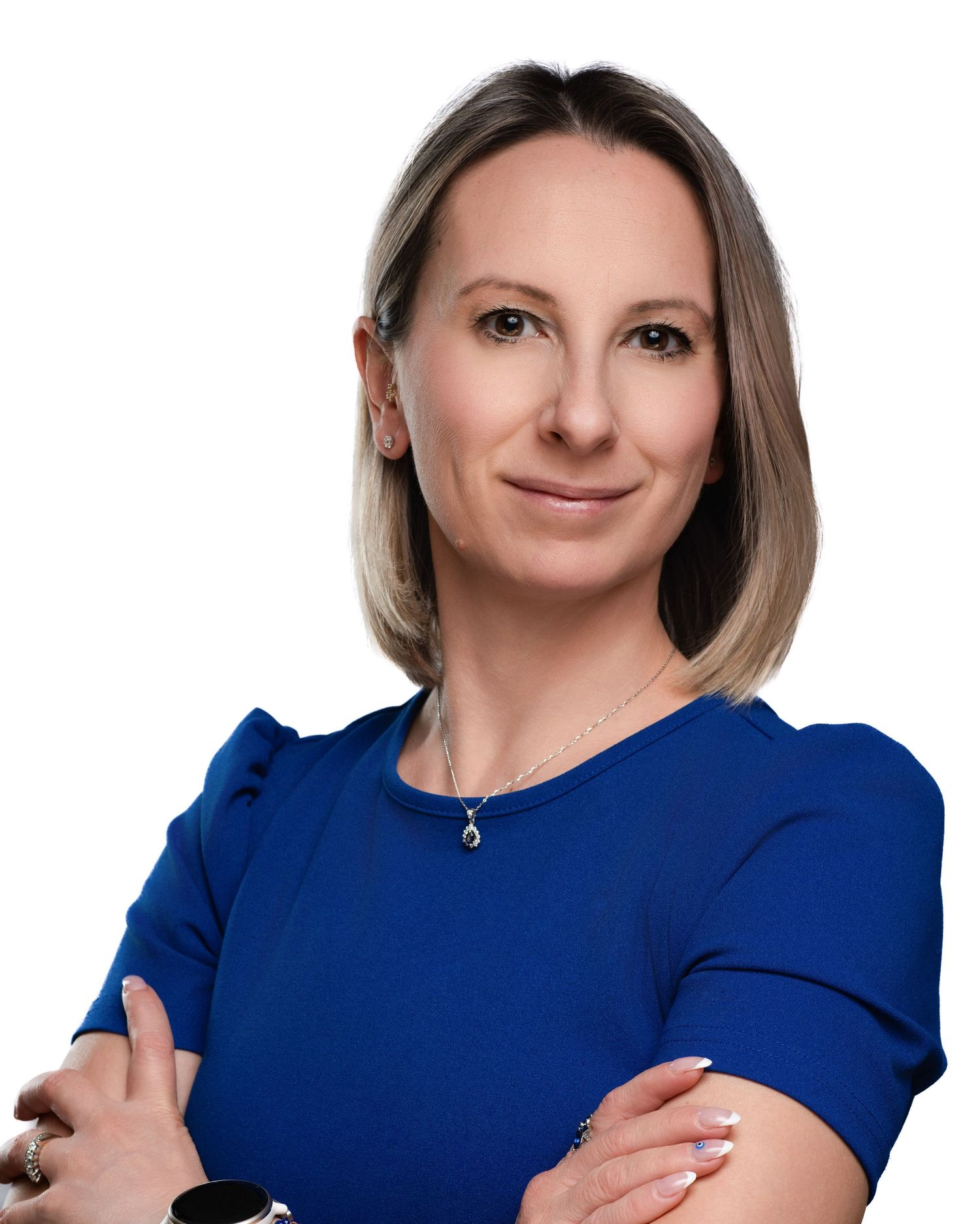Professional portrait of someone in a royal blue blouse with crossed arms and a delicate necklace against a light background.