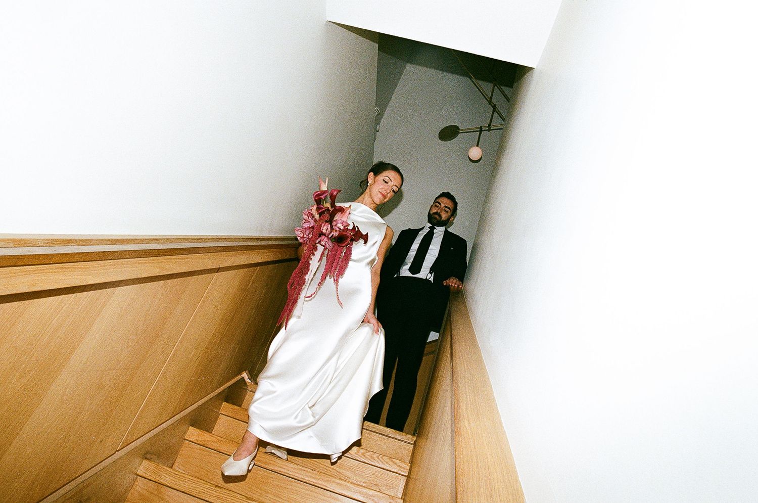 A wedding couple poses for pictures in a curved wooden hallway with beige walls and minimal lighting.