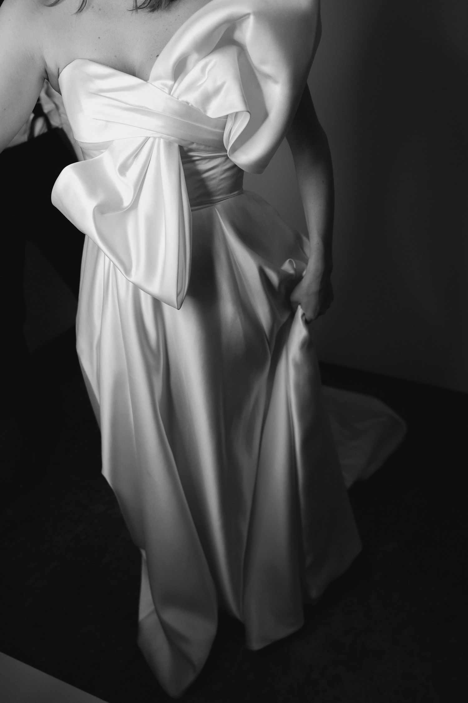 Elegant black and white photograph of a wedding dress with dramatic draping and oversized bow detail.