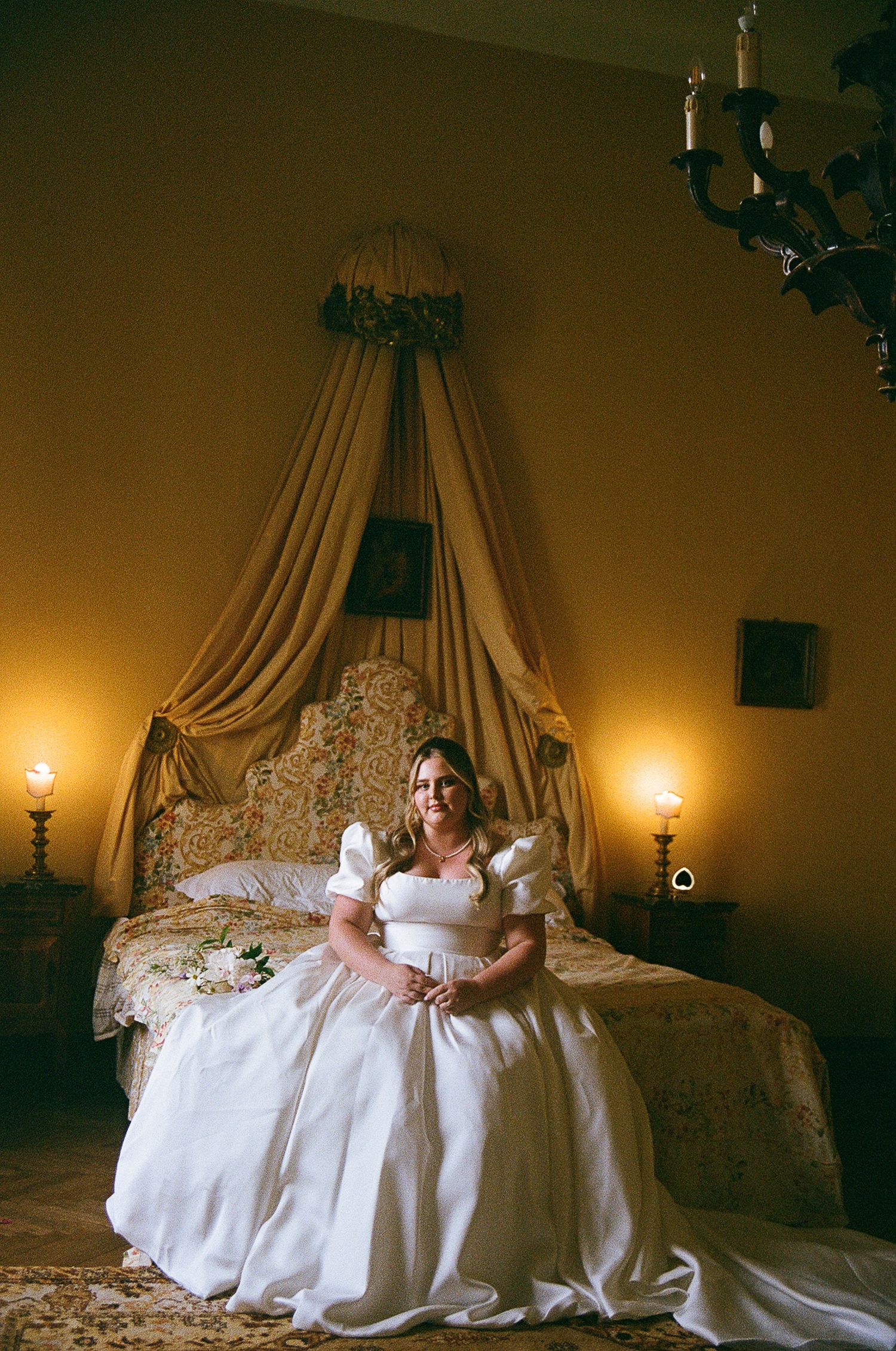 An elegant white bridal gown flowing across an ornate bed with dramatic lighting and drapery.