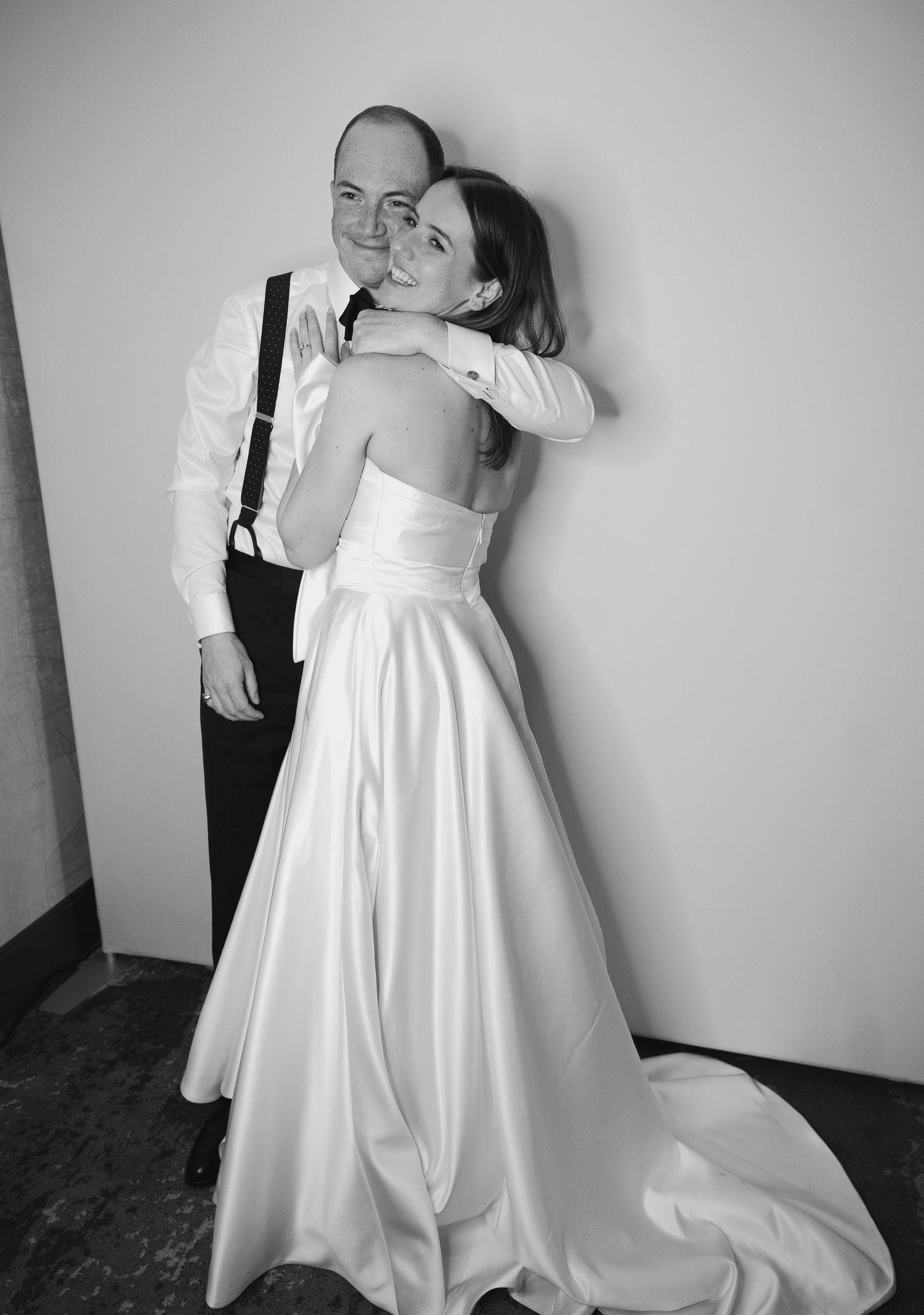 Couple embracing in formal attire, with bride wearing elegant white gown with train in black and white photo.