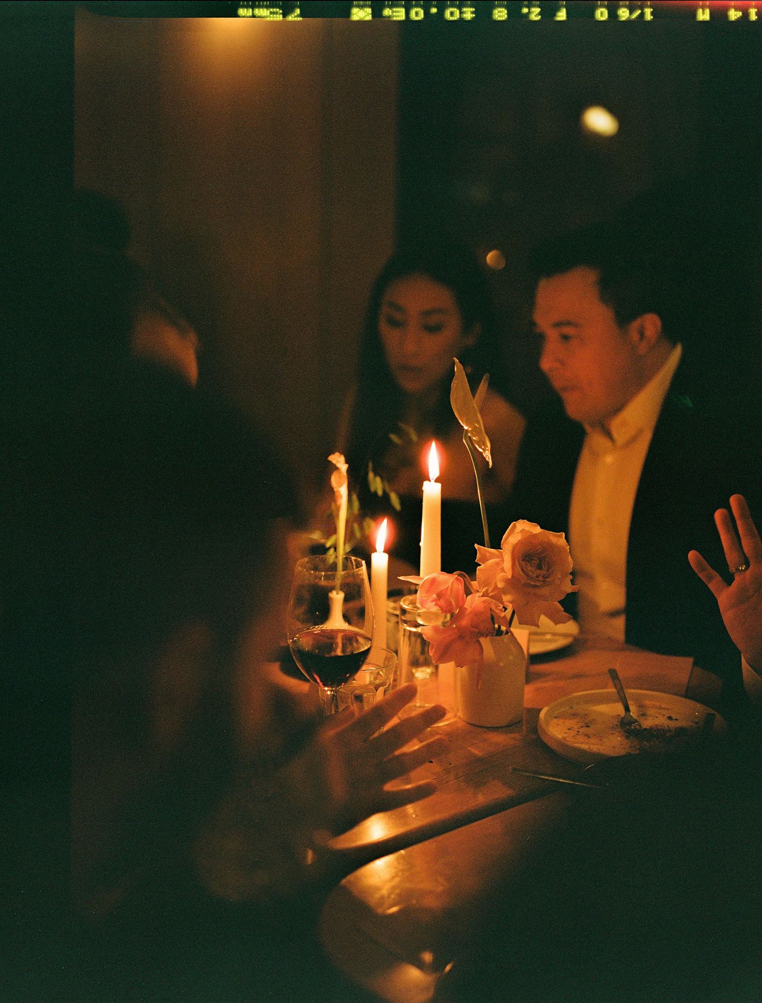 Diners share an intimate candlelit dinner with wine glasses and candles creating a warm, romantic ambiance.