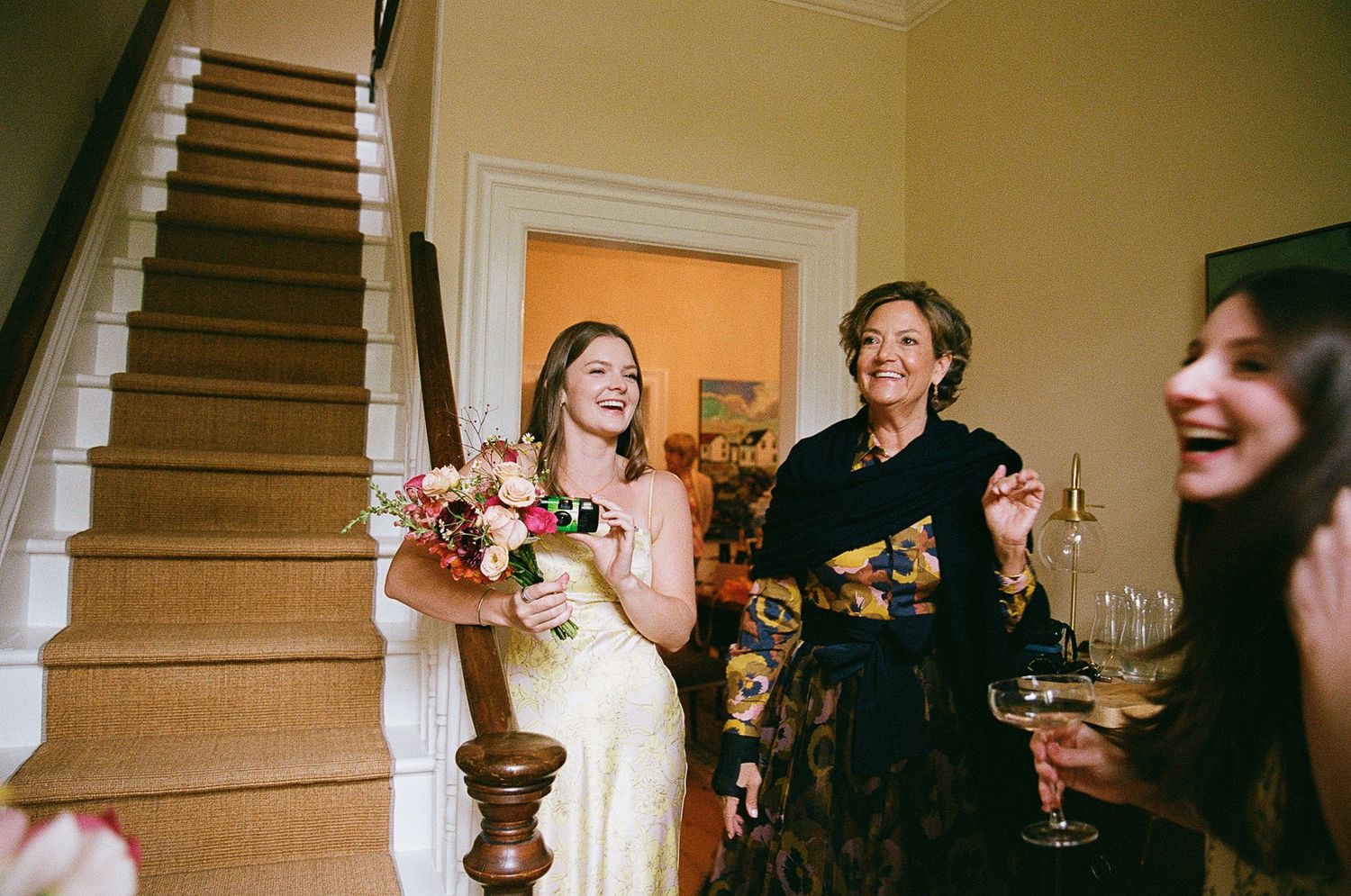 People laughing and socializing at a candlelit dinner party beside a wooden staircase.