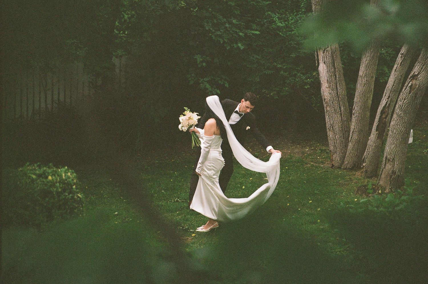 A romantic wedding moment captured in a lush green garden as flowing white dress and veil create ethereal movement.
