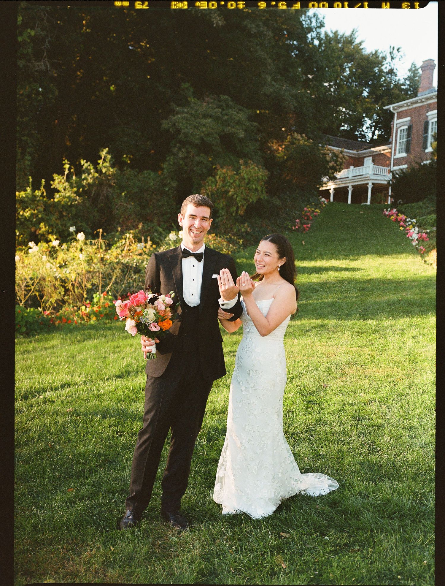 A couple shares a happy moment on their wedding day standing in the sunlit garden of an elegant estate property.