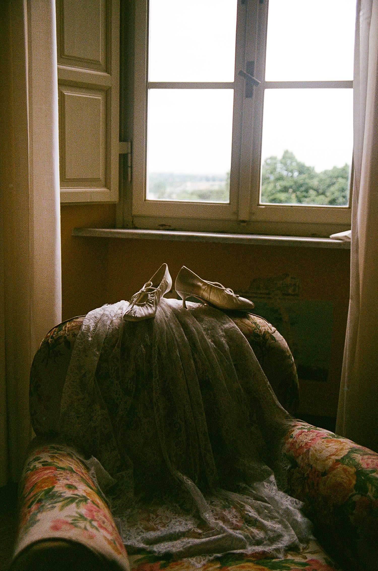 An old floral armchair sits by a window in moody natural lighting creating a vintage atmospheric scene.