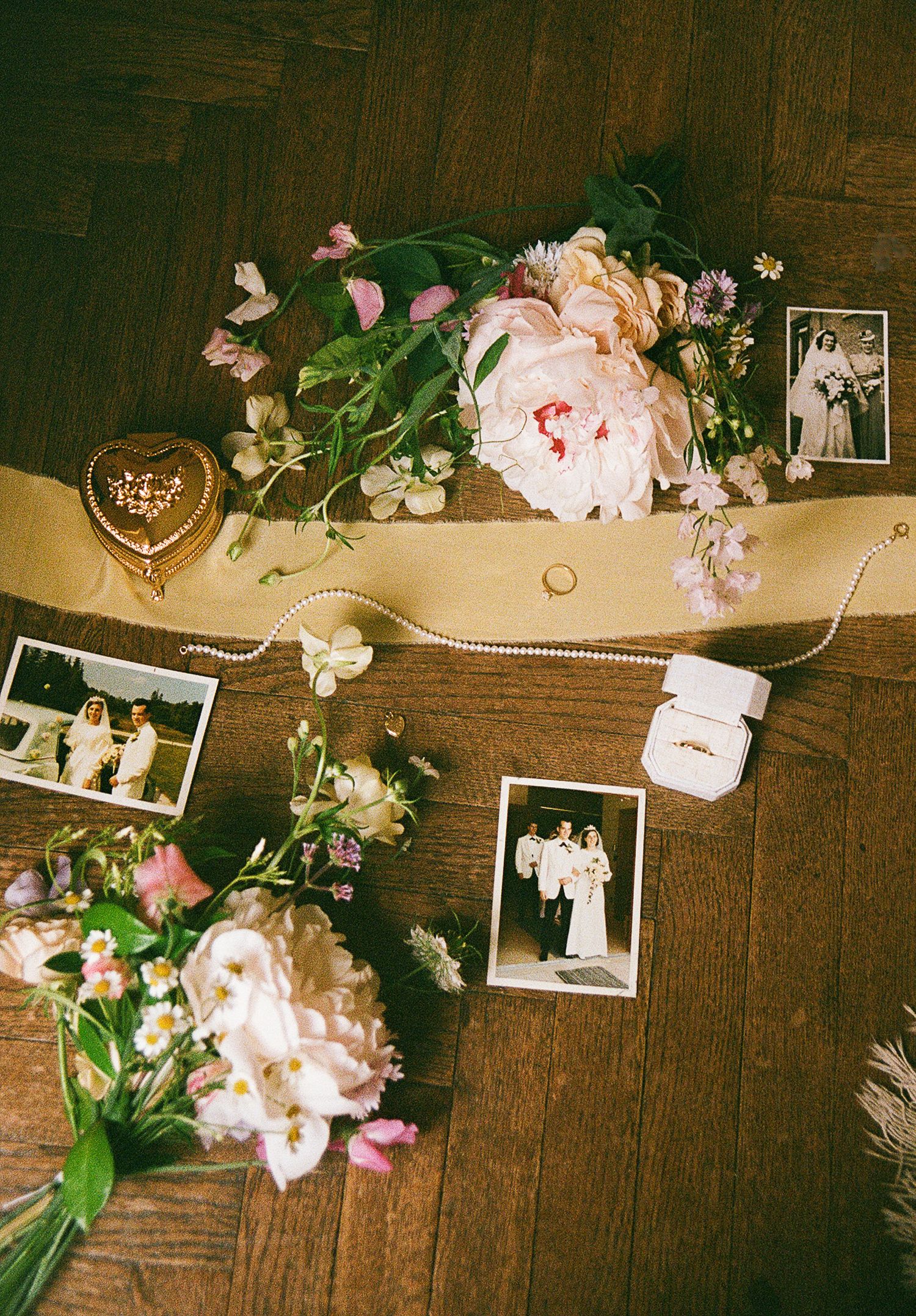 Vintage wedding photos displayed on wooden surface with delicate pink peonies and pearl string decorations.