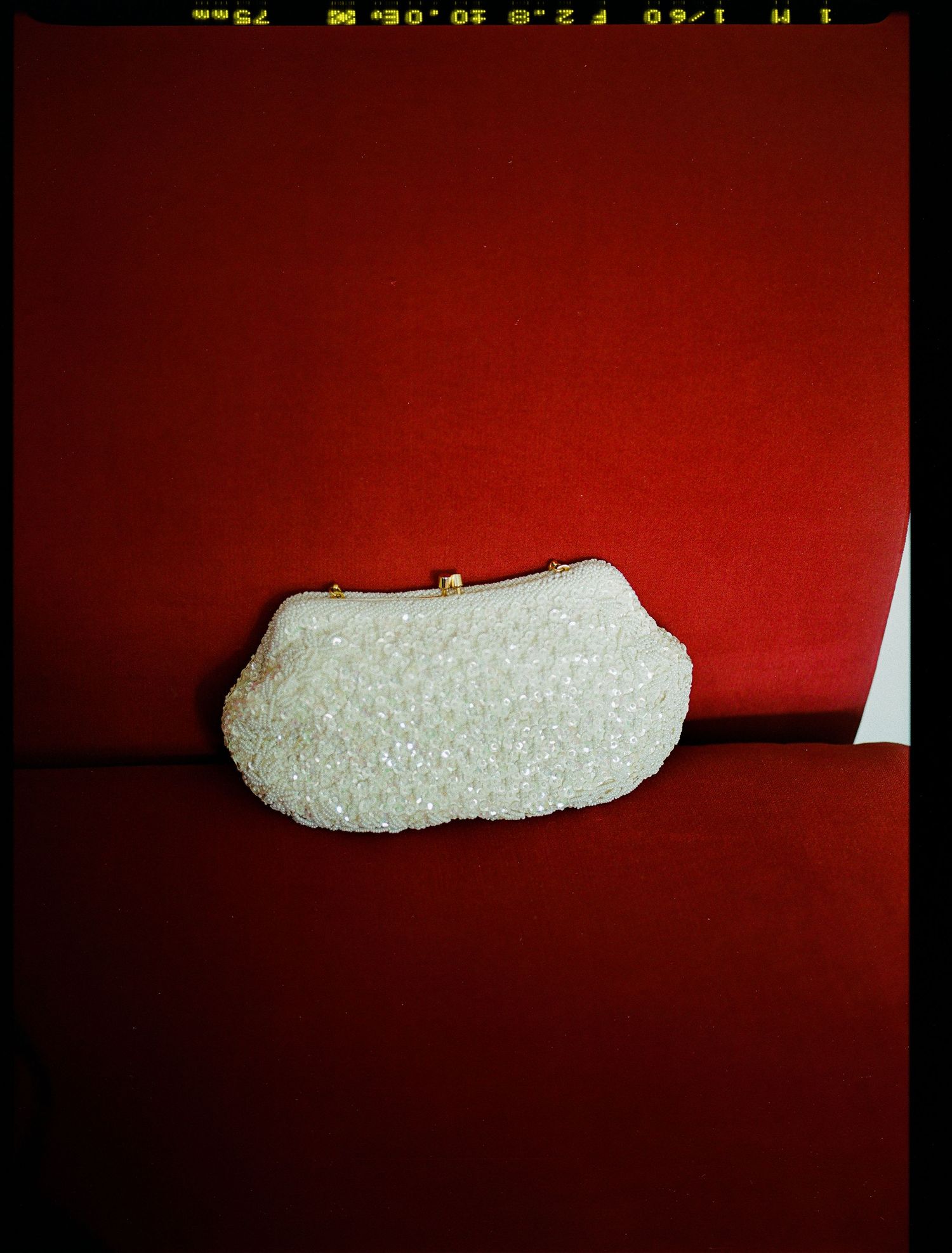 A white beaded evening clutch purse sits elegantly against a deep red background.