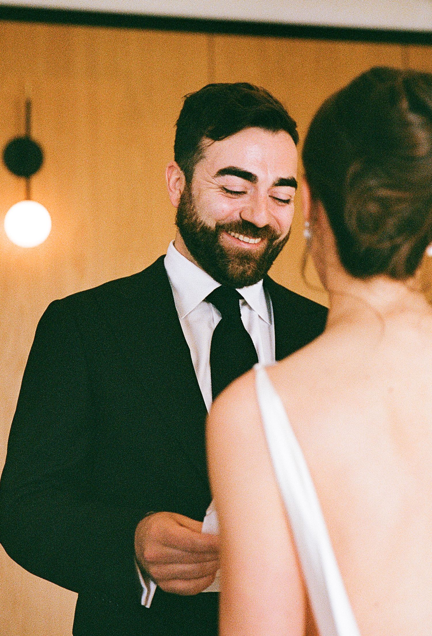 A heartwarming candid moment at a wedding showing joyful expressions against a warm-toned indoor backdrop.