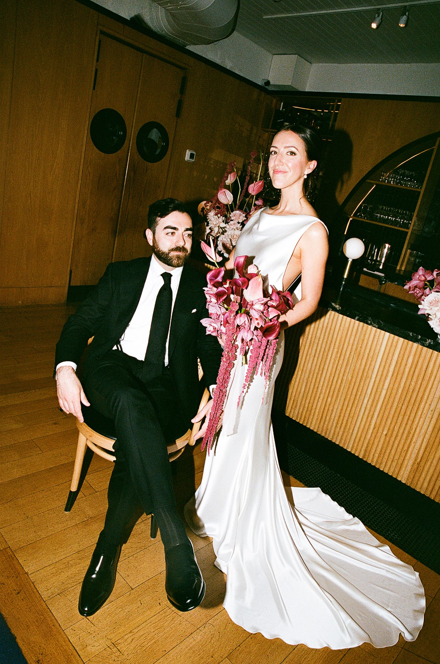 Couple performs playful dance moves during their wedding reception in a wood-paneled venue.