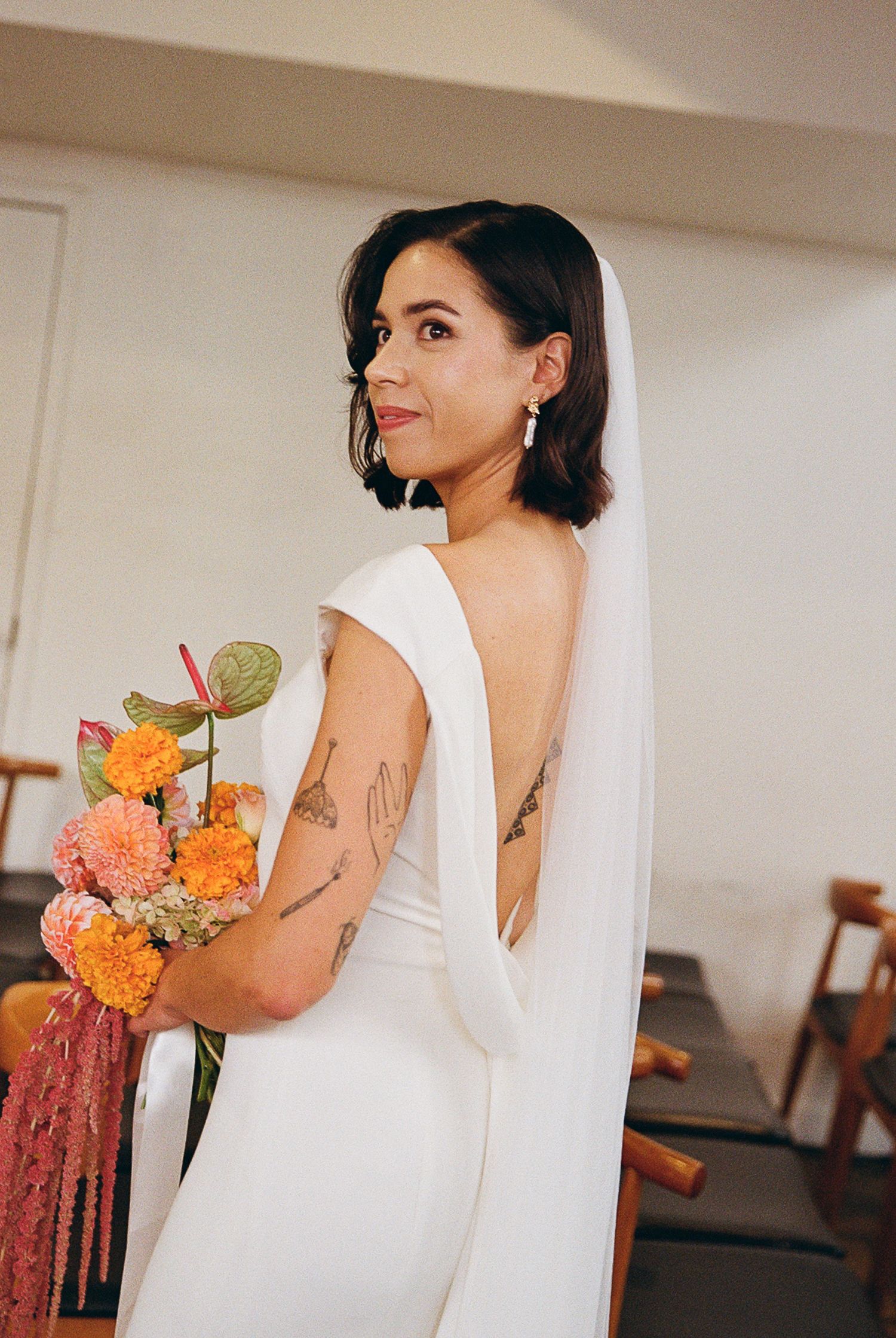 A bride in a classic white v-back wedding dress holds a vibrant bouquet of orange and coral flowers with citrus accents.
