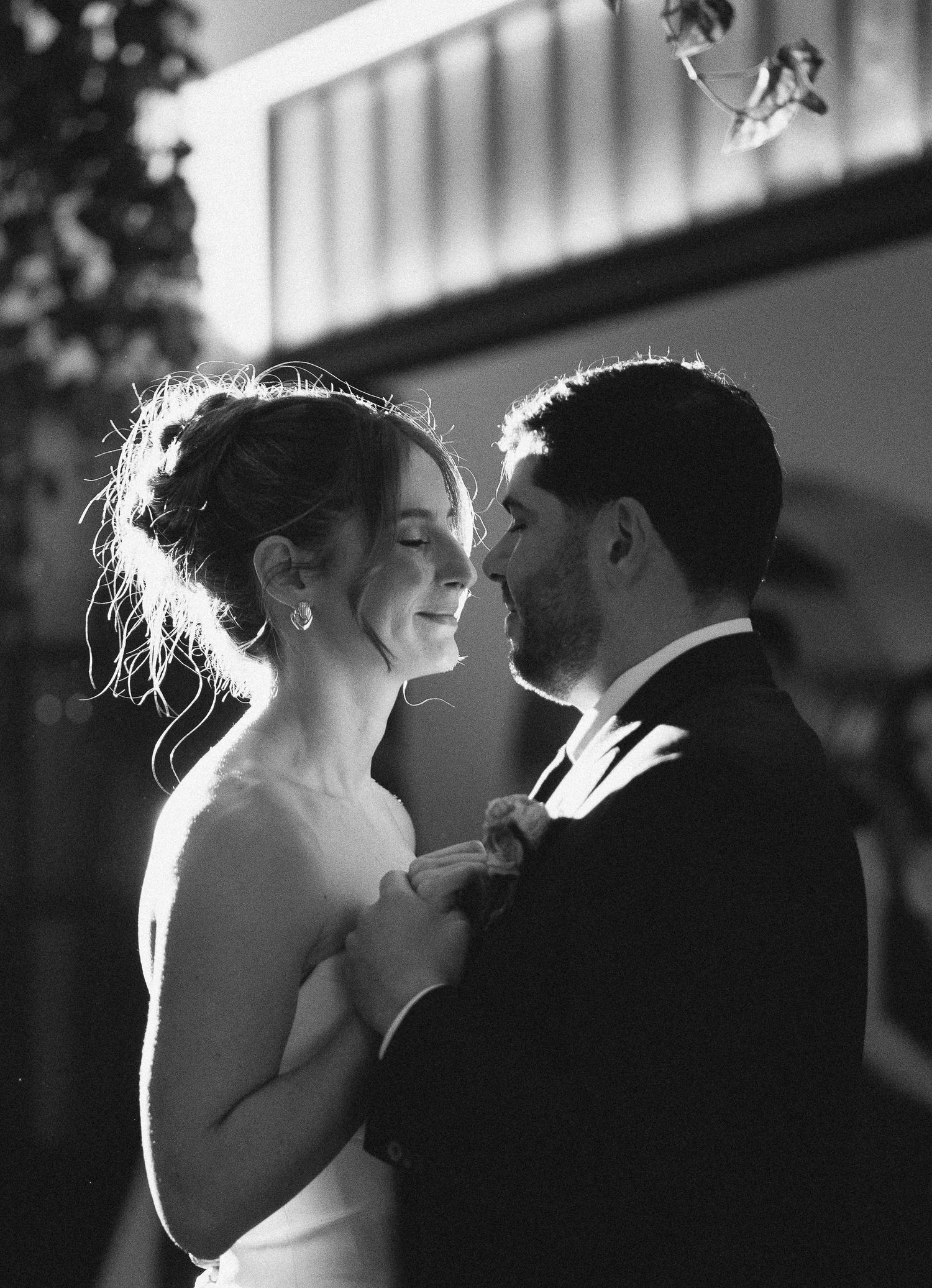 Black and white backlit silhouette photos of a romantic couple in formal attire sharing tender moments at their wedding.
