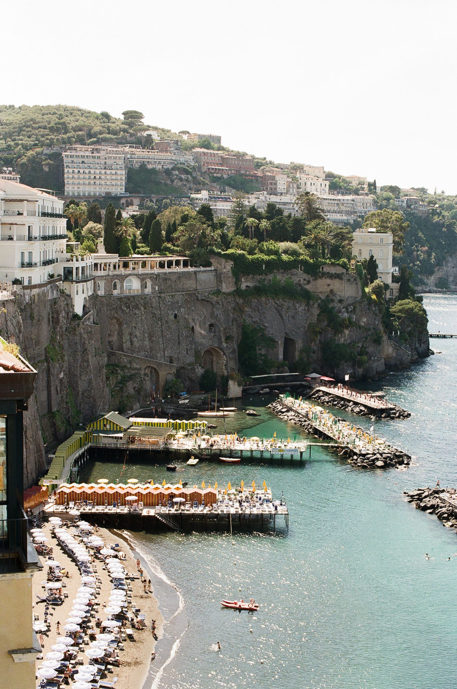 Scenic coastal view of Sorrento, Italy with cliffside buildings, beach umbrellas and turquoise Mediterranean waters.