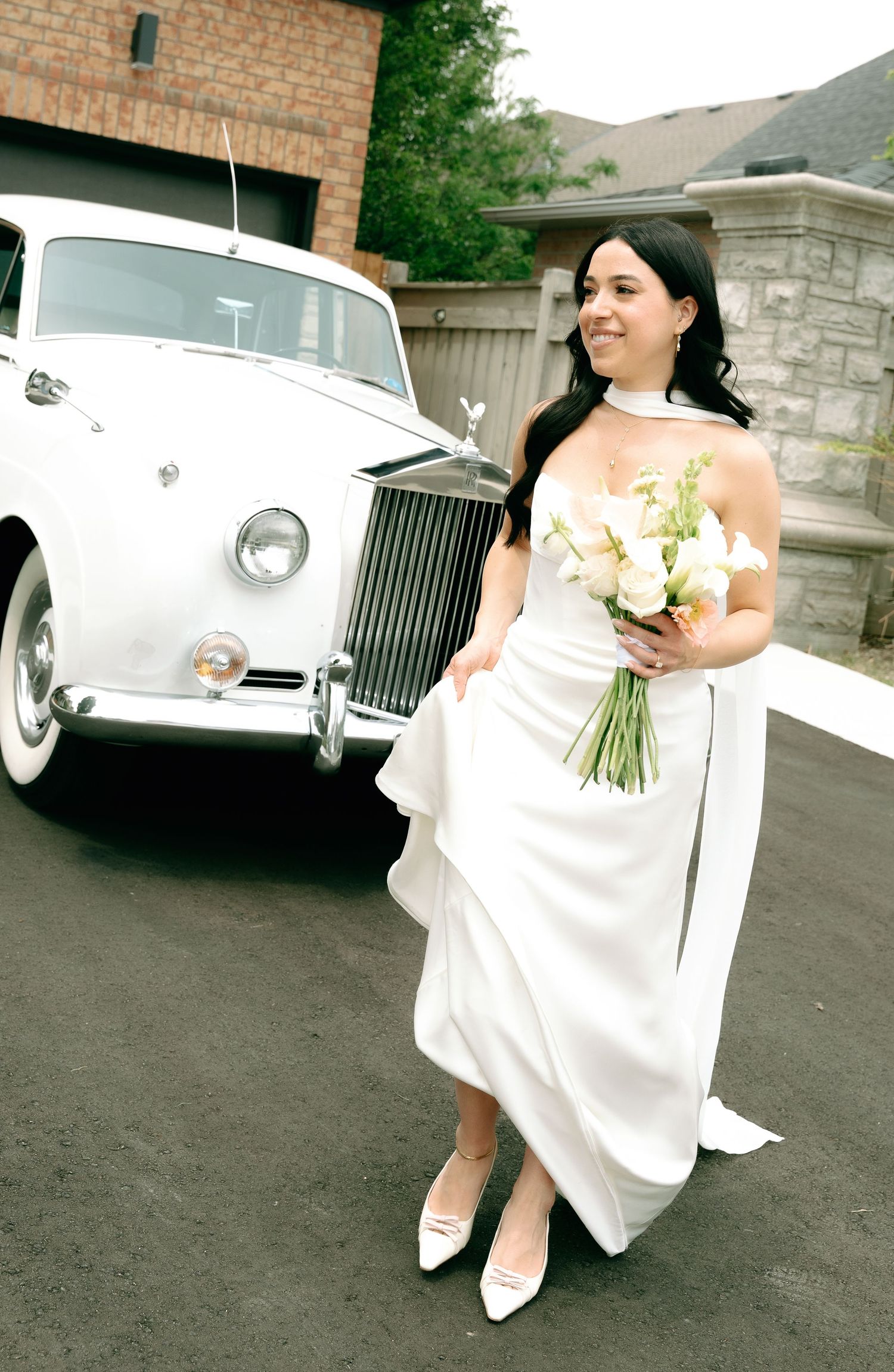 A bride in a white wedding gown stands next to a classic white Rolls Royce car in multiple artistic angles.