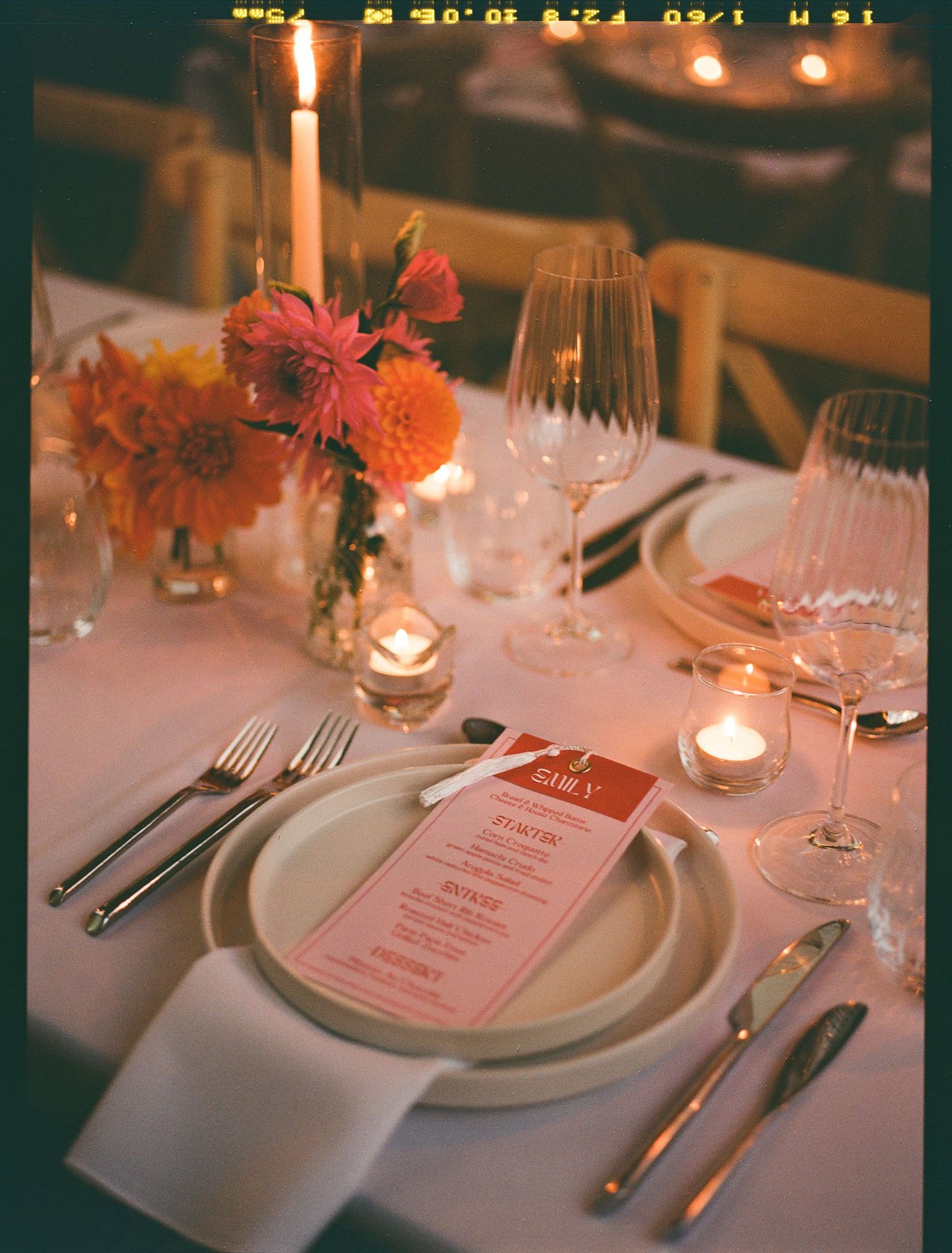 An elegant table setting with pink menu card, floral centerpiece, glowing candles, and wine glasses for fine dining.