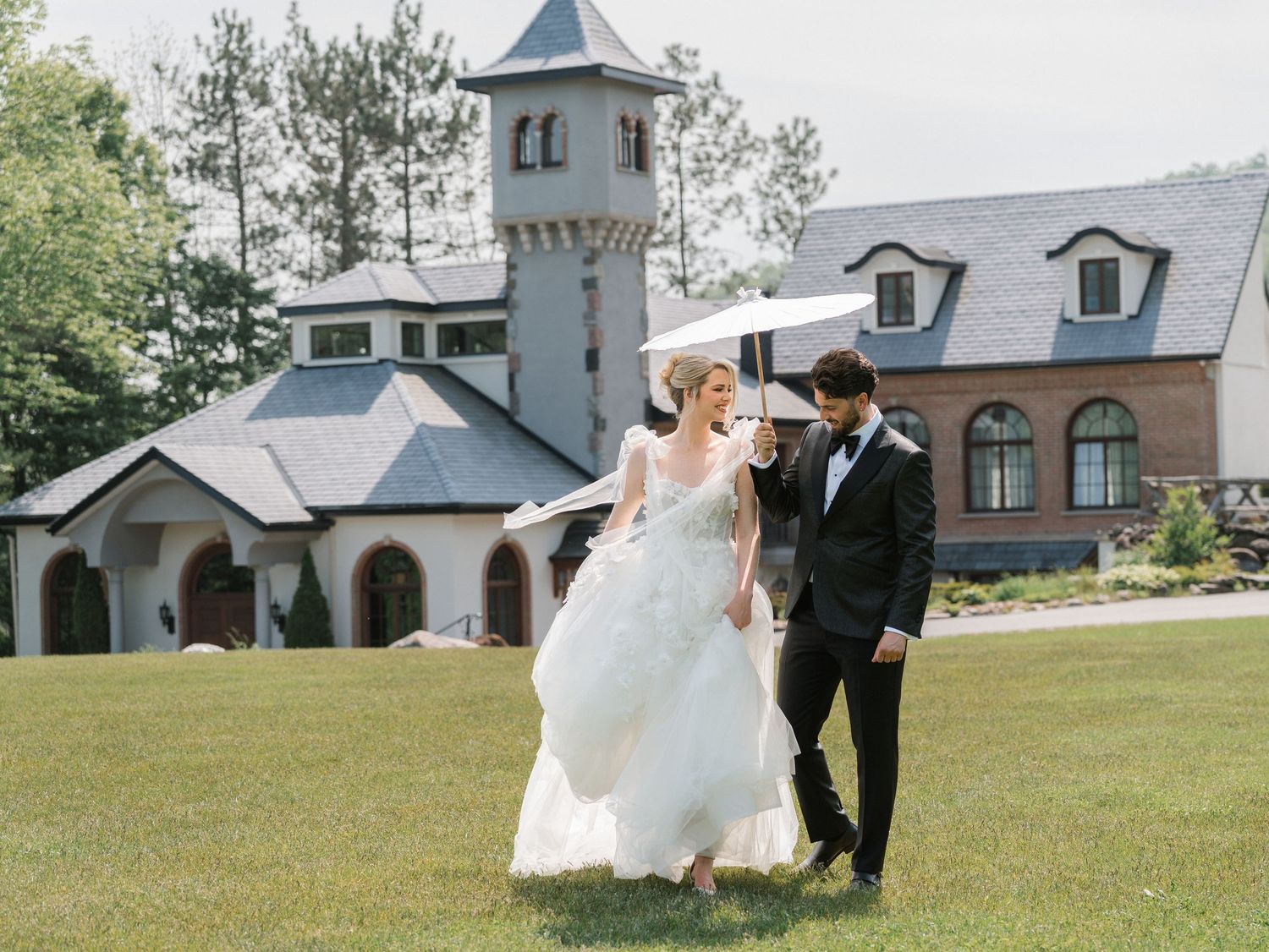 Wedding couple strolling on lawn in front of stone chapel with tower.