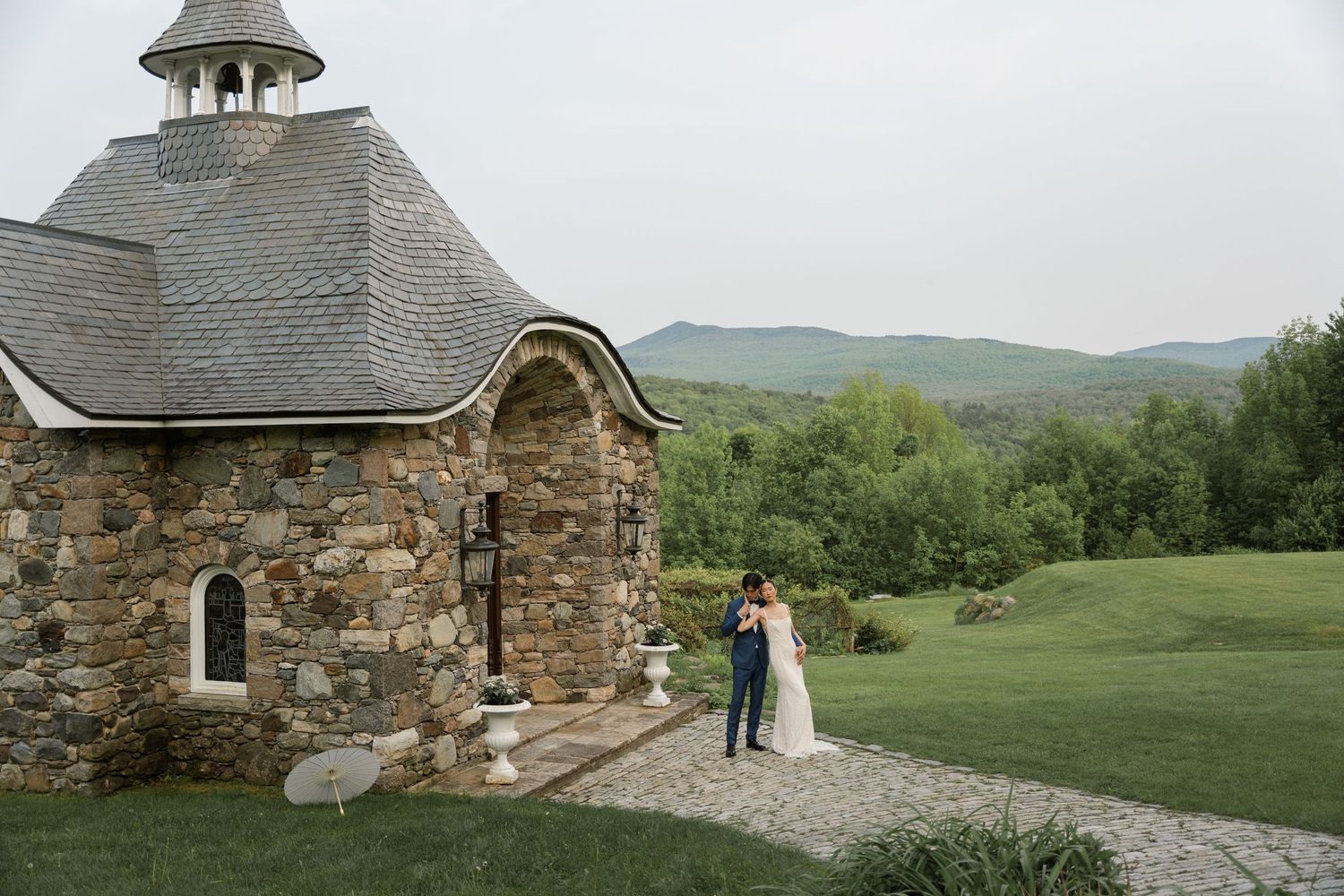 Stone chapel with unique cupola nestled among rolling hills and green landscape.