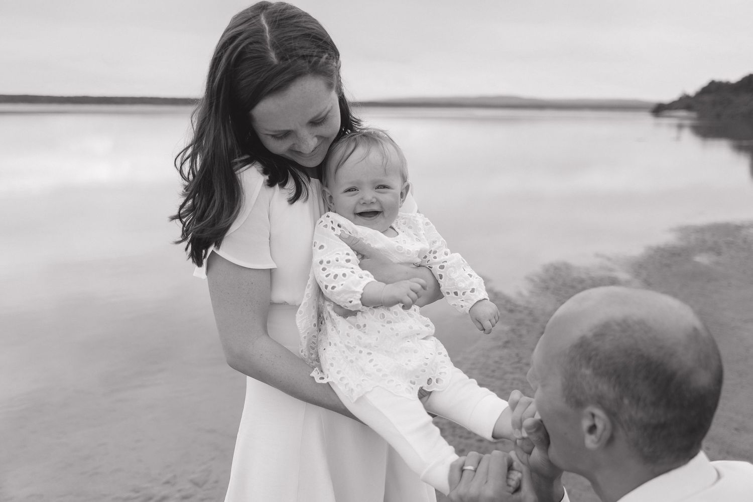 Family shares a tender moment on a beach at sunset with water in the background.