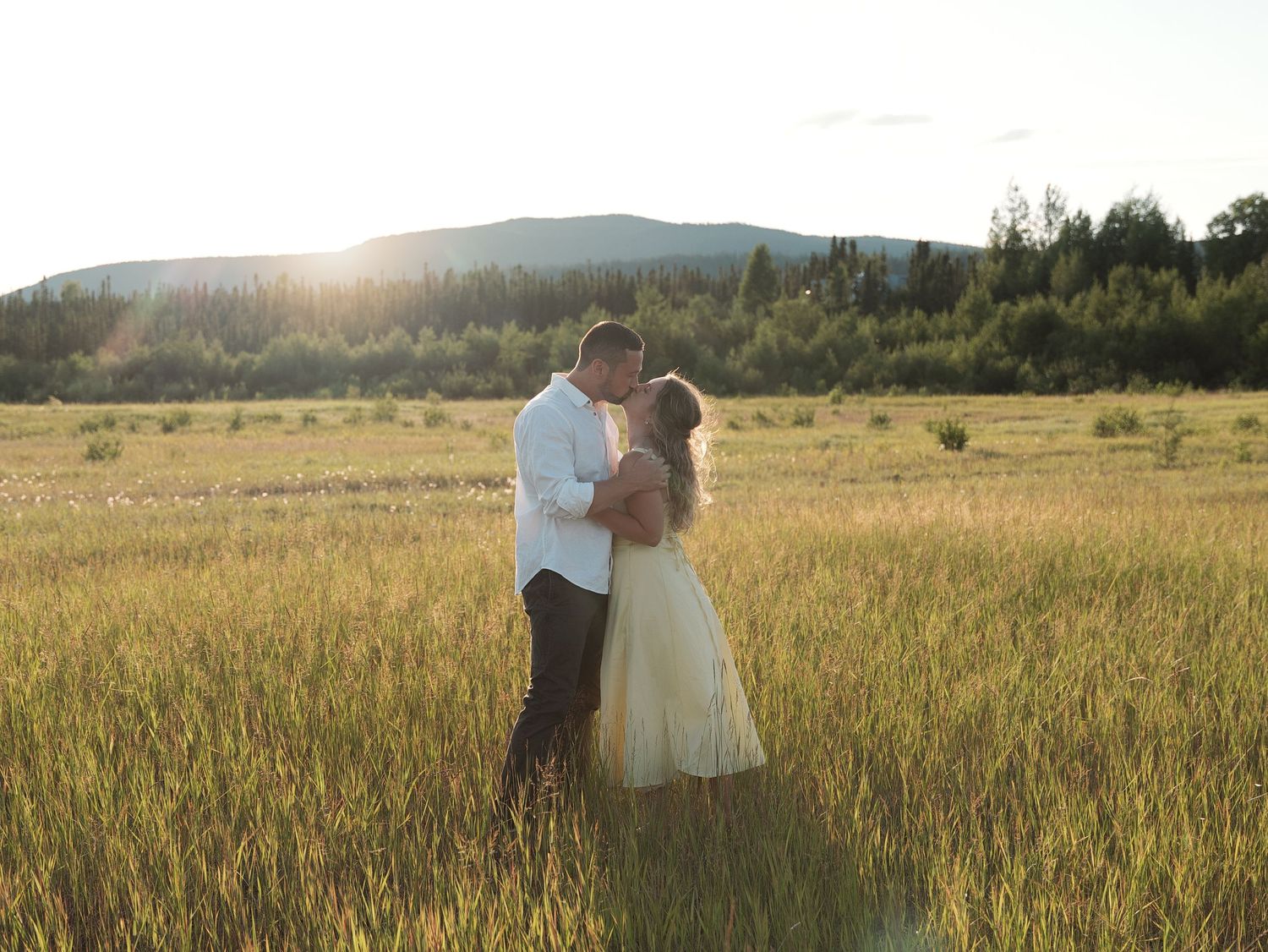 Couple walking through golden wheat field at sunset holding hands.