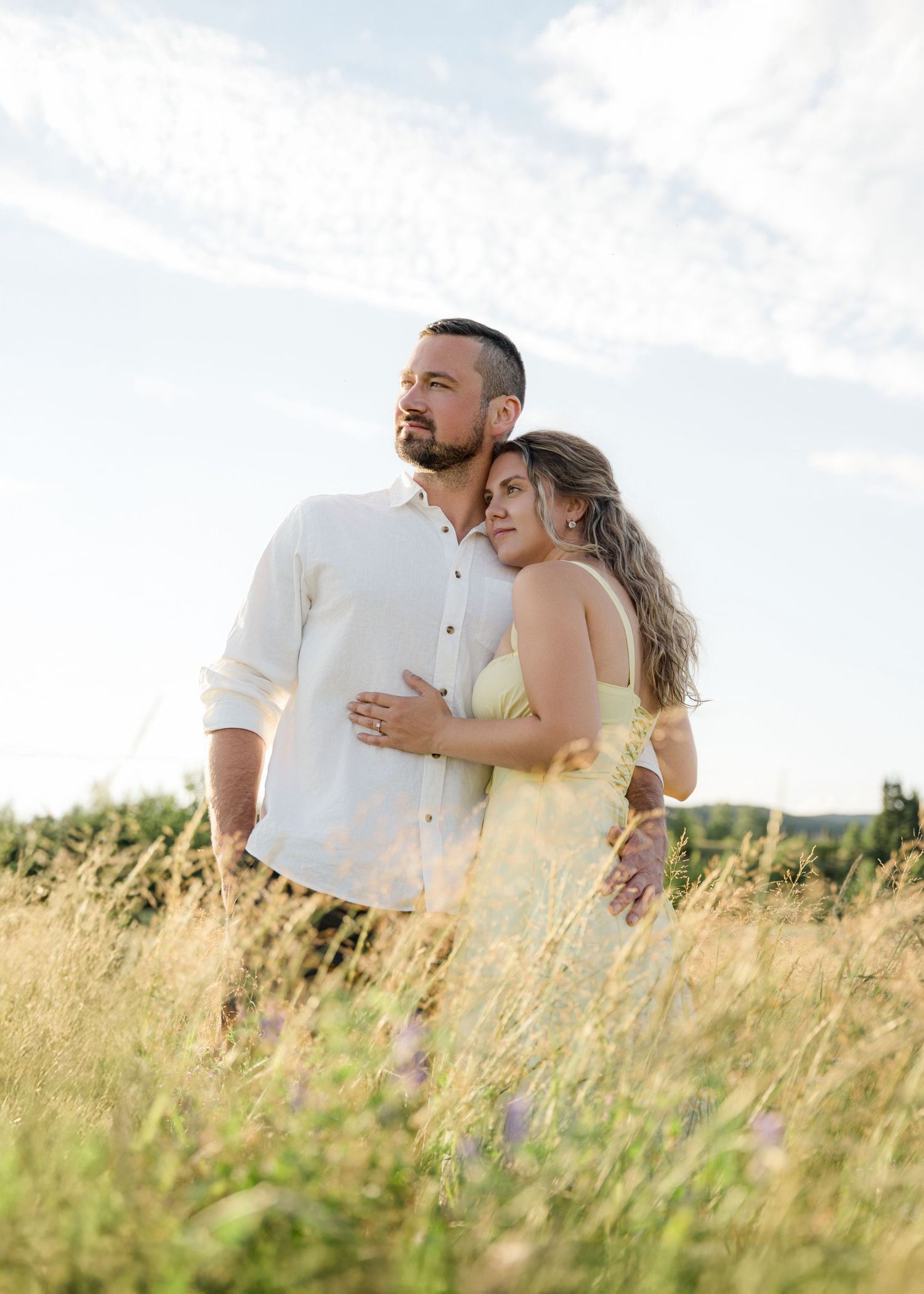 Couple embracing and laughing together in tall summer grass field.