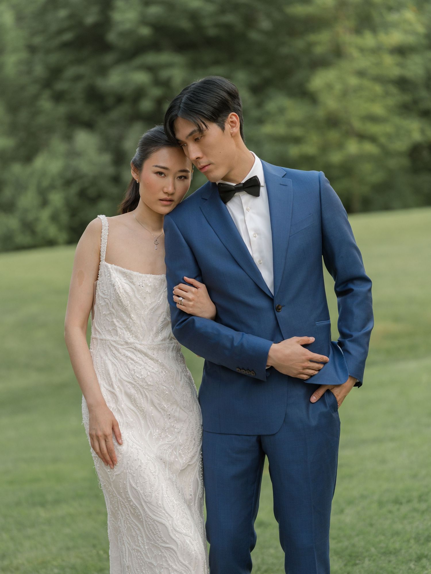 Wedding couple in traditional attire posing together on green grass.