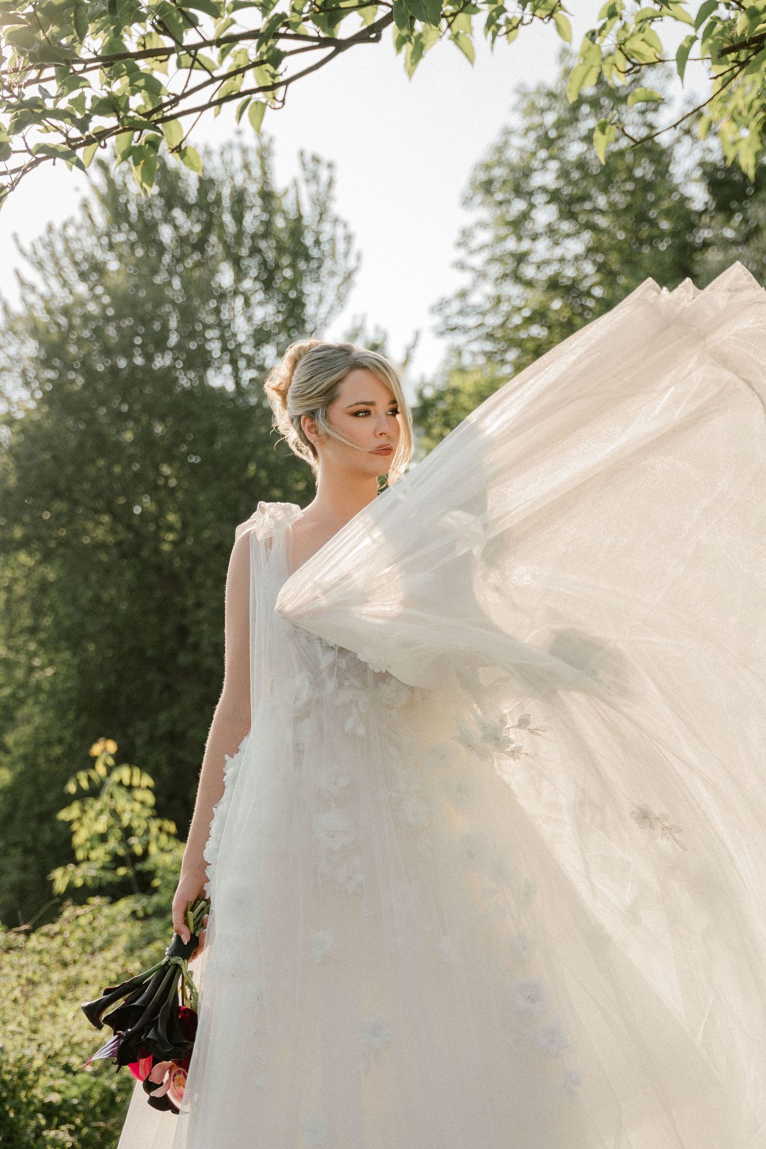 Flowing white wedding dress fabric caught in natural sunlight among trees.