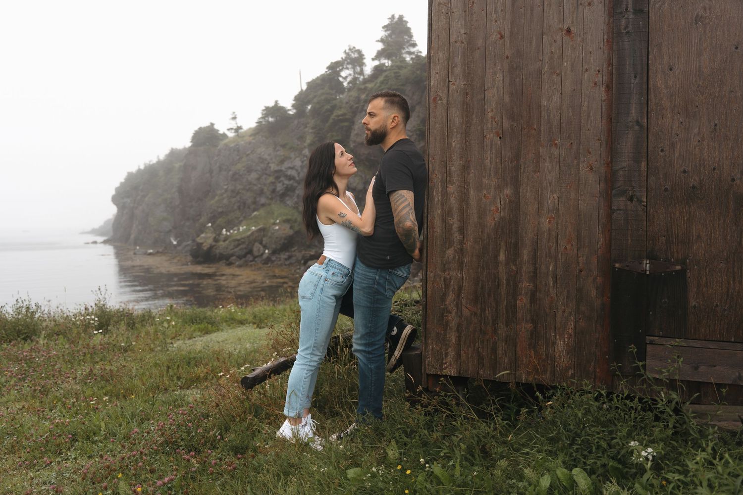 A series of romantic outdoor portraits show a couple embracing against a rustic wooden barn wall in a misty countryside setting.