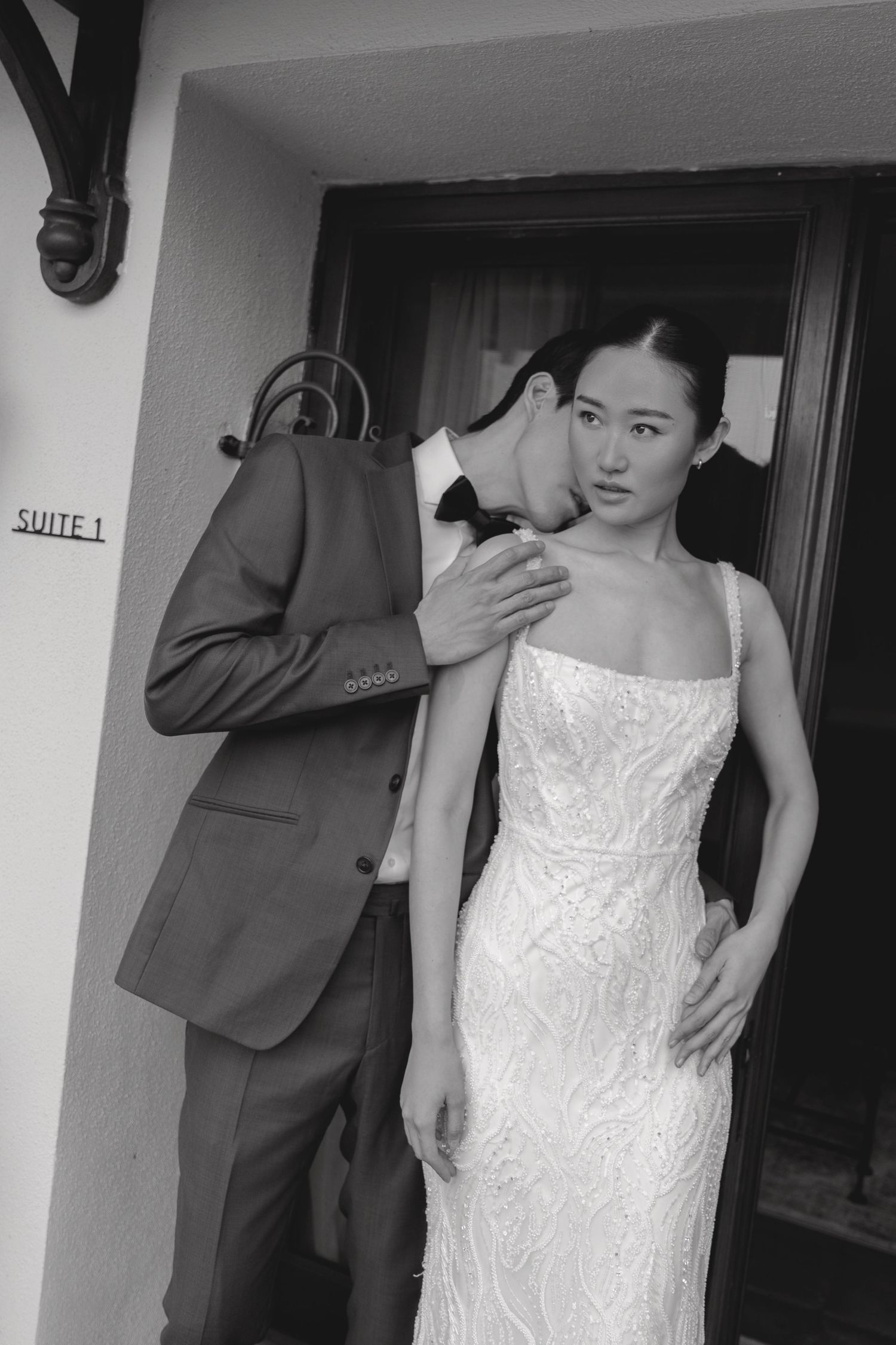 Black and white photo of woman in lace dress standing next to suit-wearing figure.