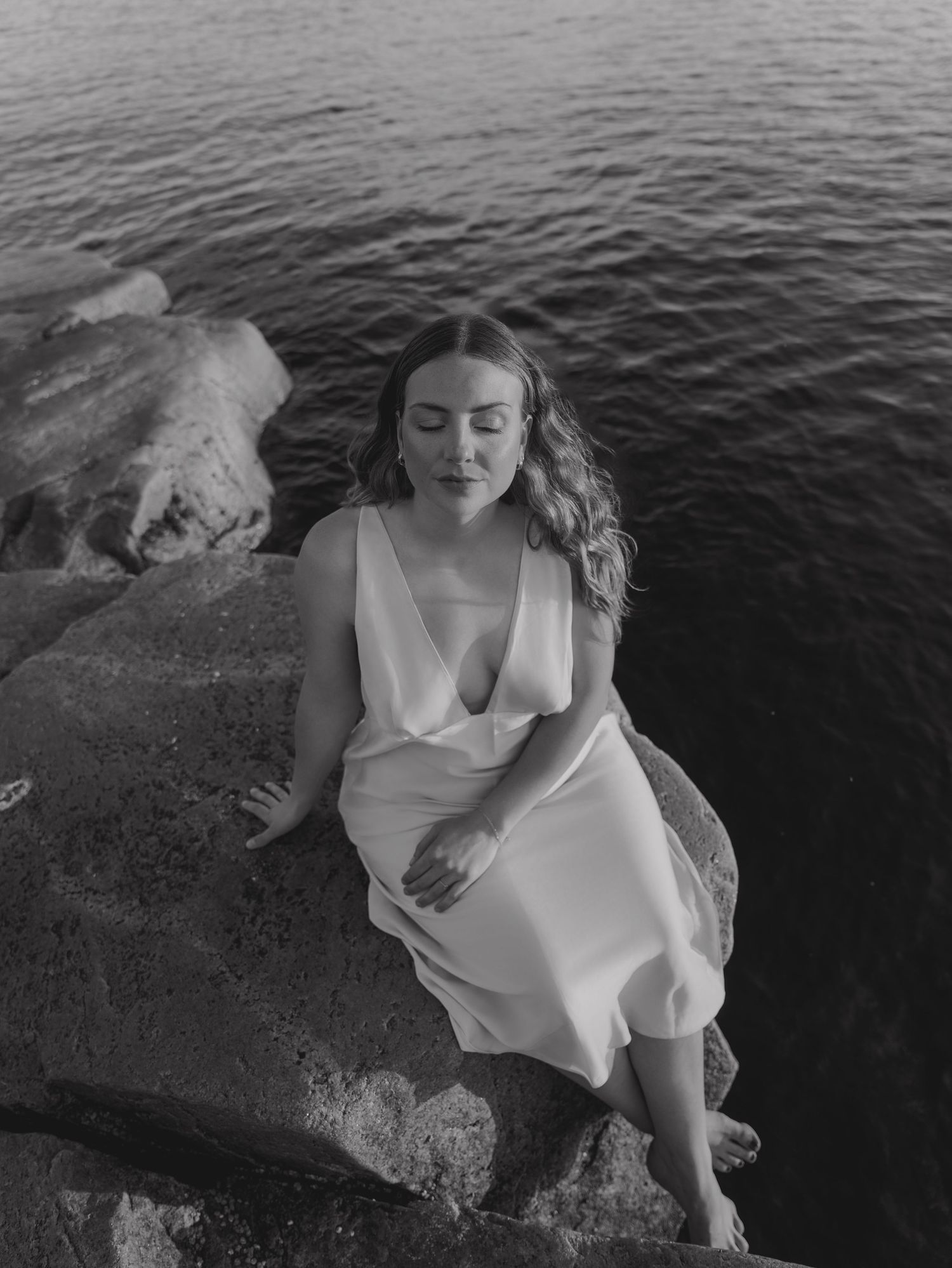 Artistic black and white portraits on dark rocks against deep water.