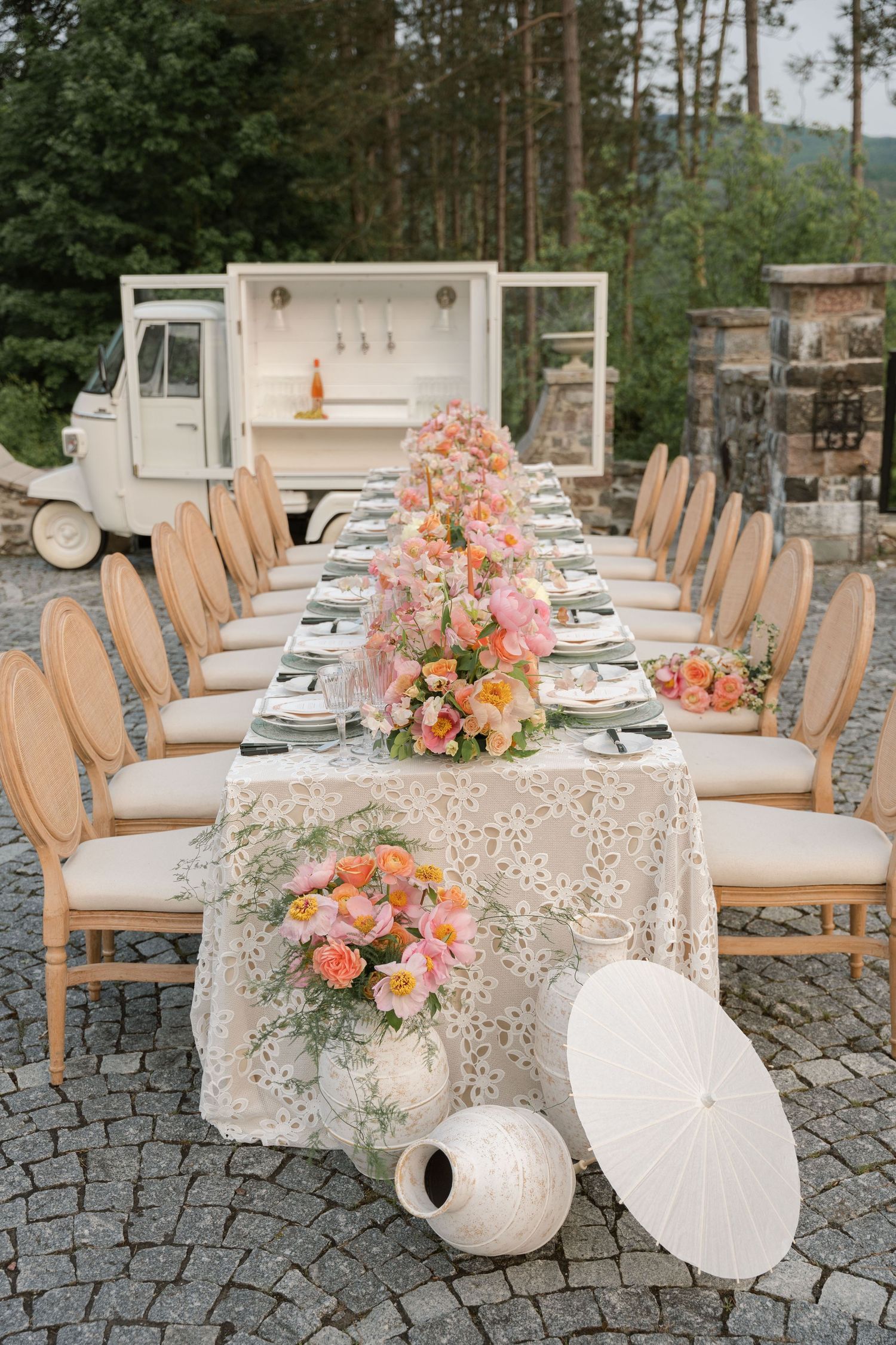 Outdoor wedding reception setup with lace tablecloths and coral flower arrangements.