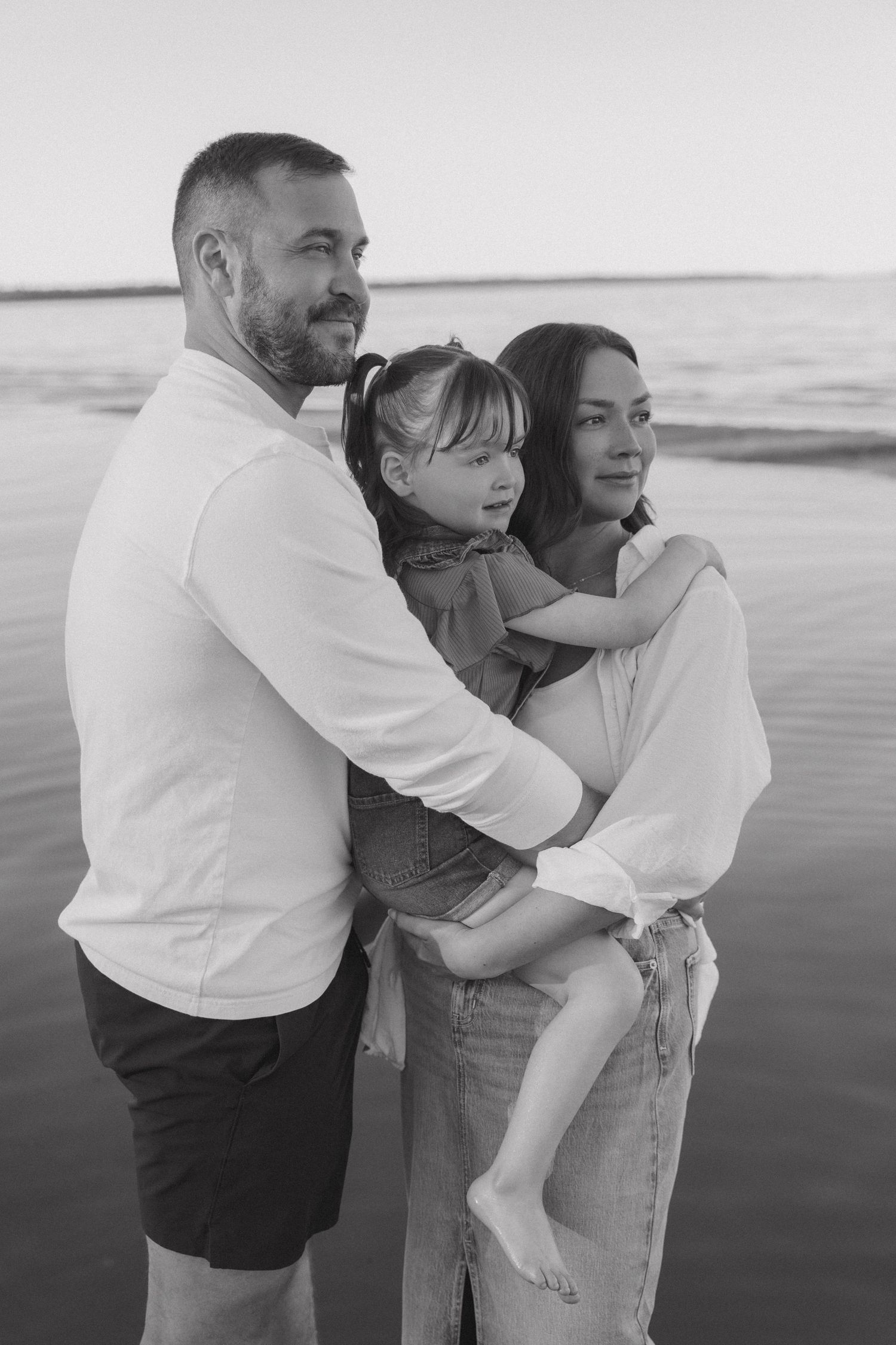 Family sharing tender moment together at beach during sunset in black and white.