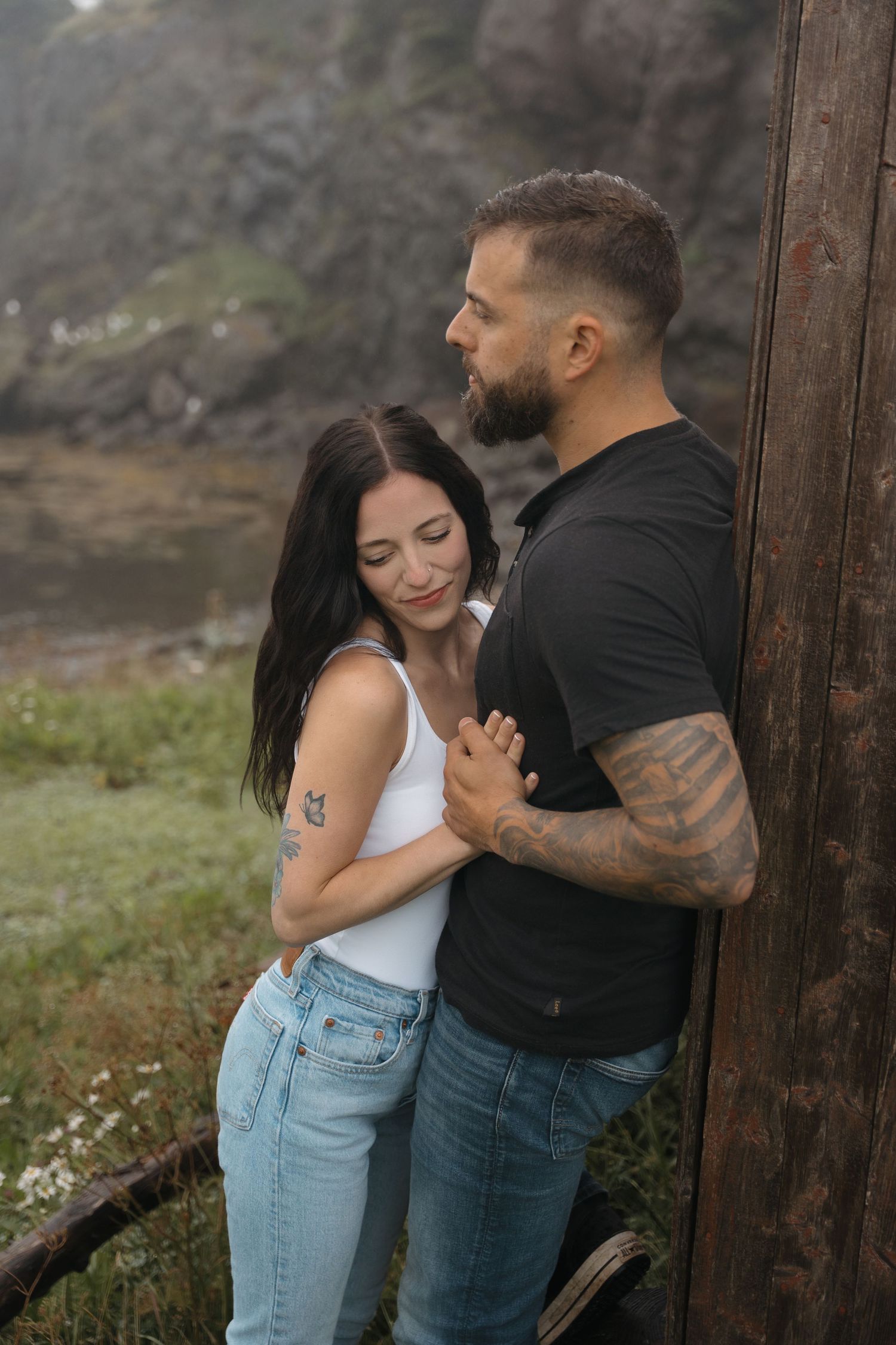 Intimate couple moment against rustic outdoor setting with mountains and greenery in background.