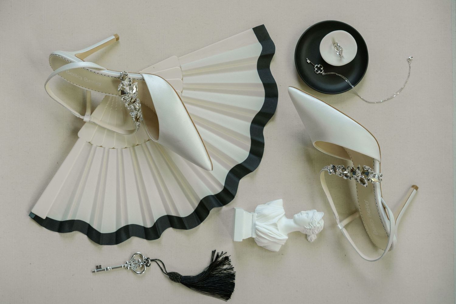 Wedding accessories including white fan, jewelry and decorative tassels arranged on light background.