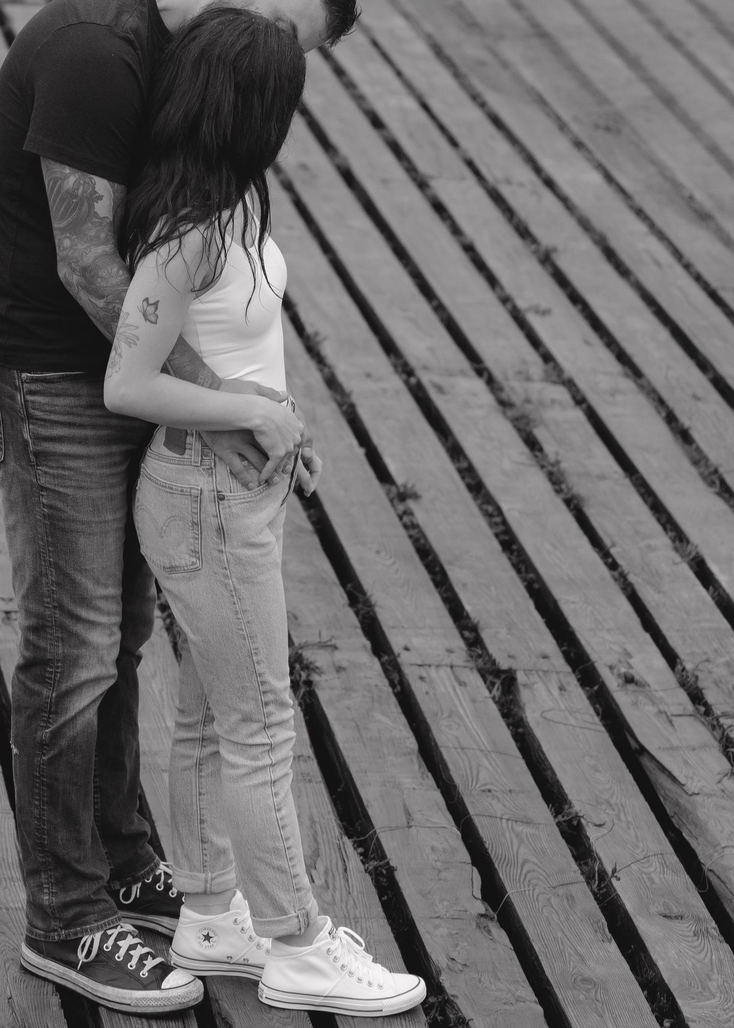 A person's feet wearing black jeans and white sneakers facing someone in white sneakers and light colored jeans.