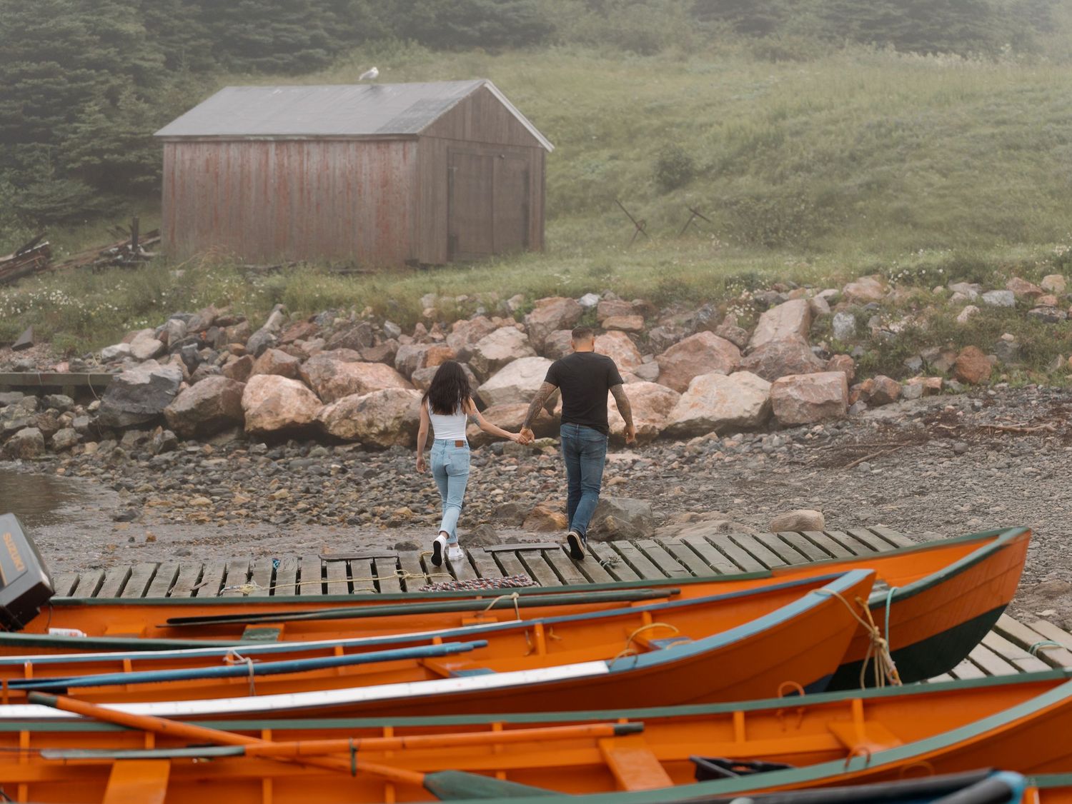 A series of bright orange kayaks lined up on a rustic wooden dock by a rocky shoreline.