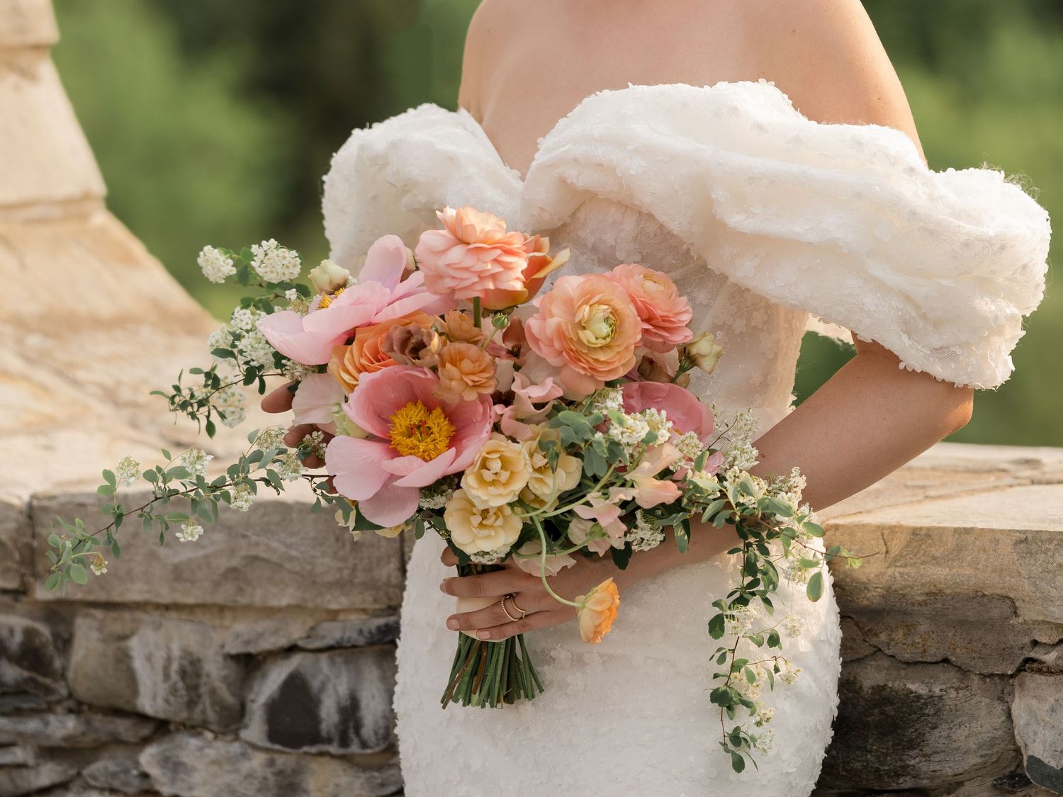 Bridal bouquet with coral and peach flowers held against white wedding dress.