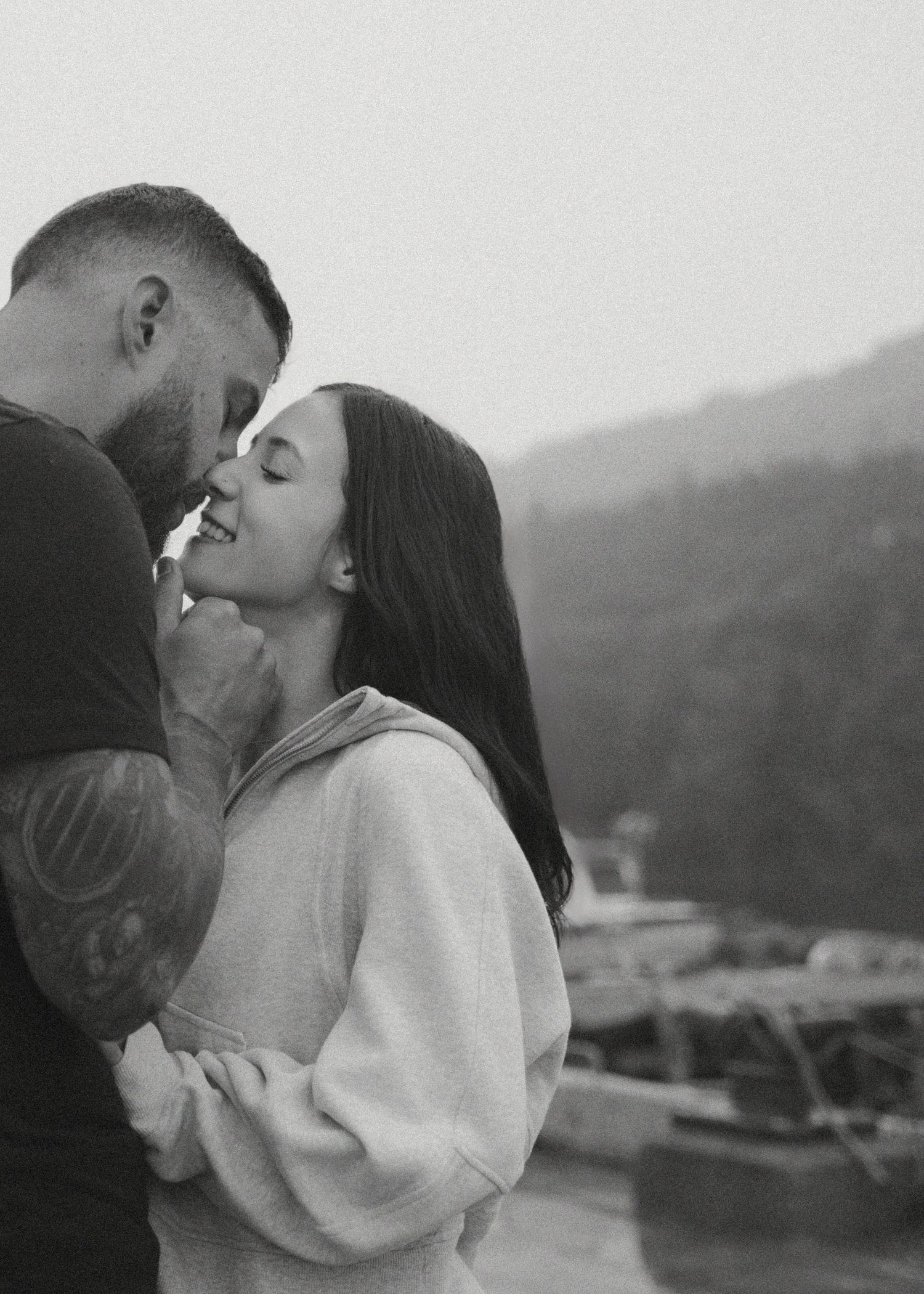 A couple shares an intimate black and white moment in profile view against a blurred background.