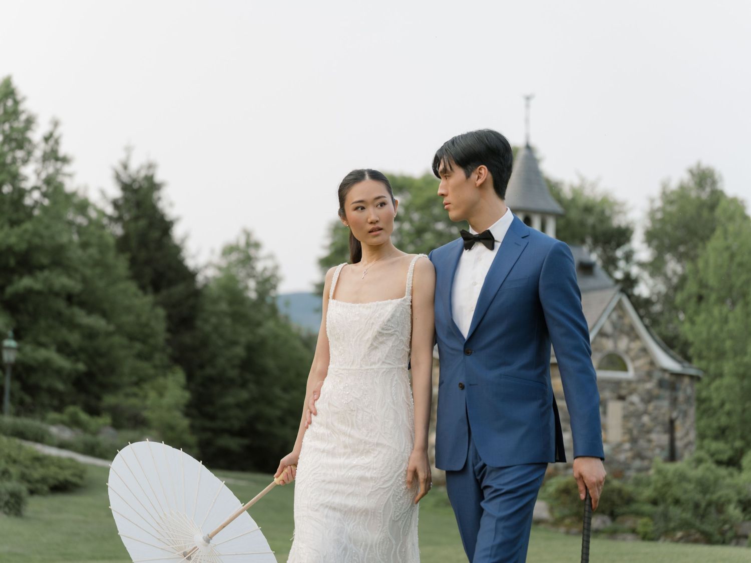Couple in formal wedding attire walking through a lush green landscape.