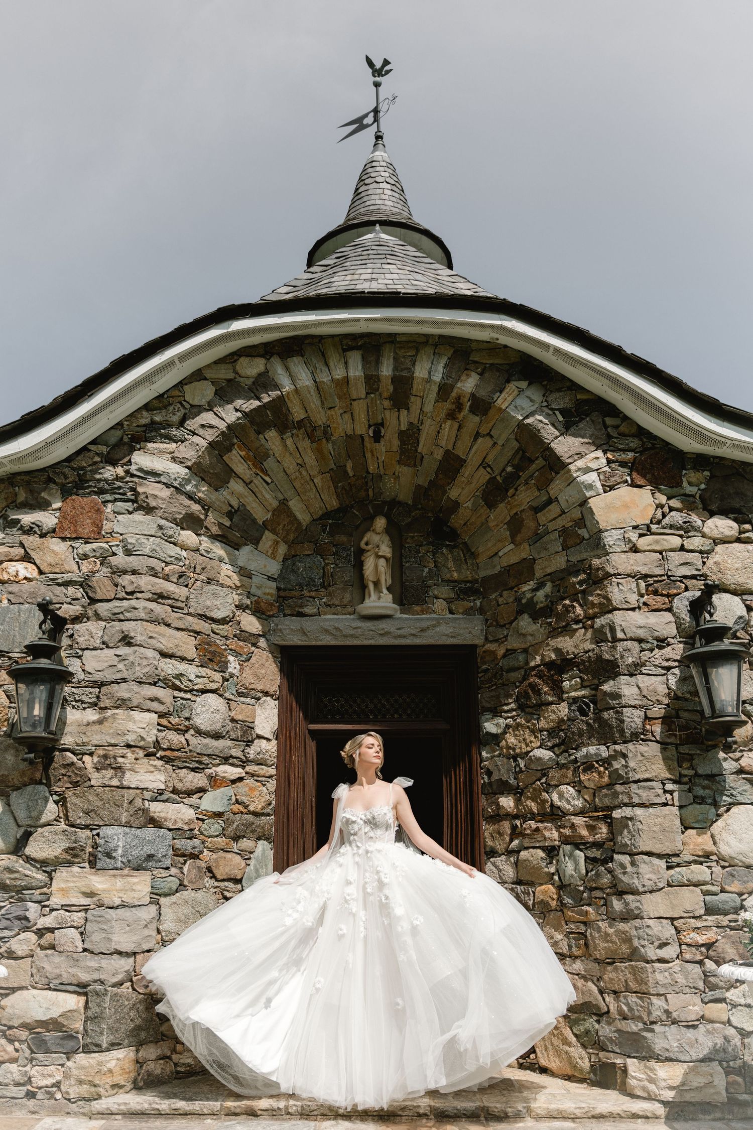 White wedding dress twirls in front of stone arch entrance with lanterns.
