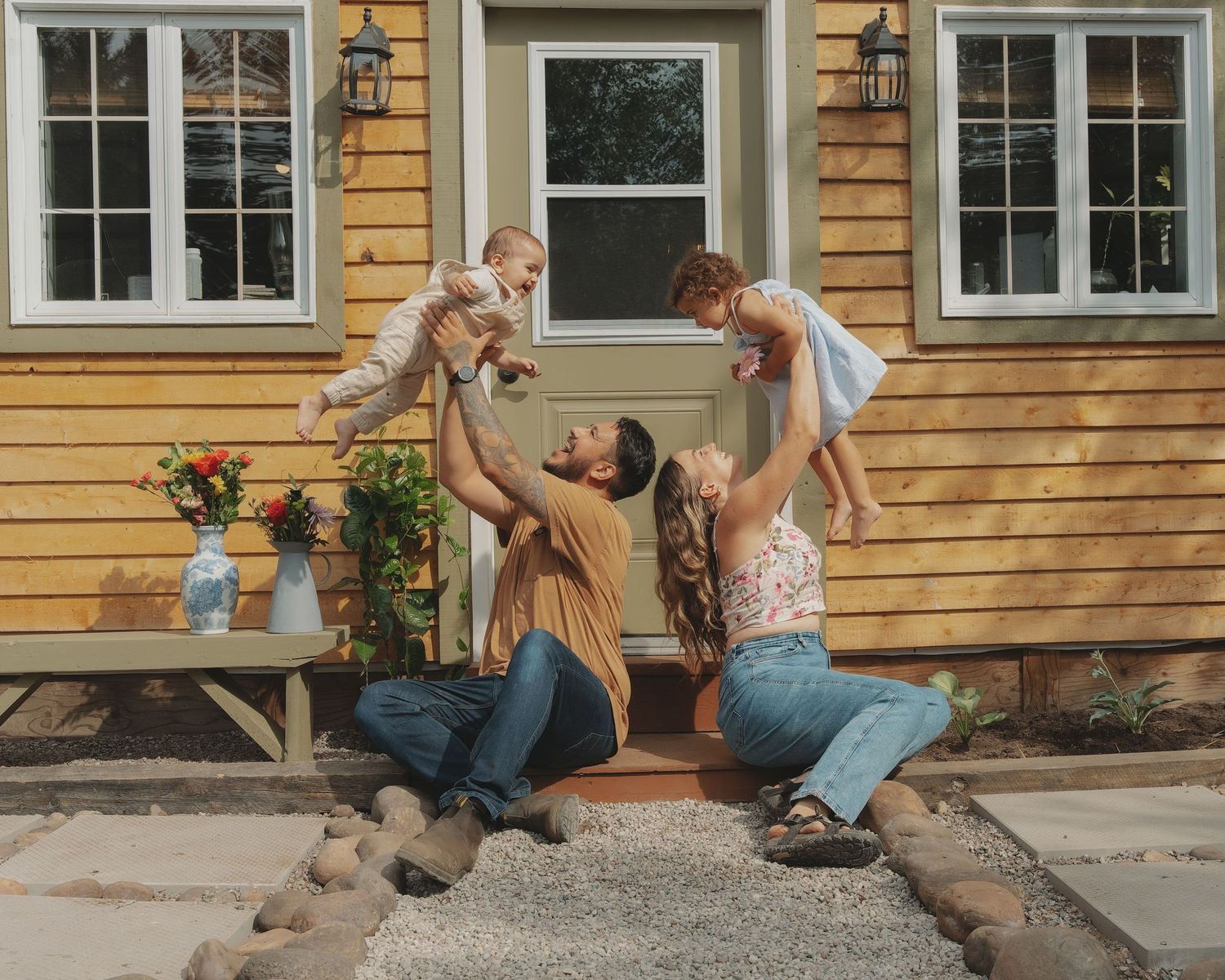 Family playing and chasing dog in front of yellow house.