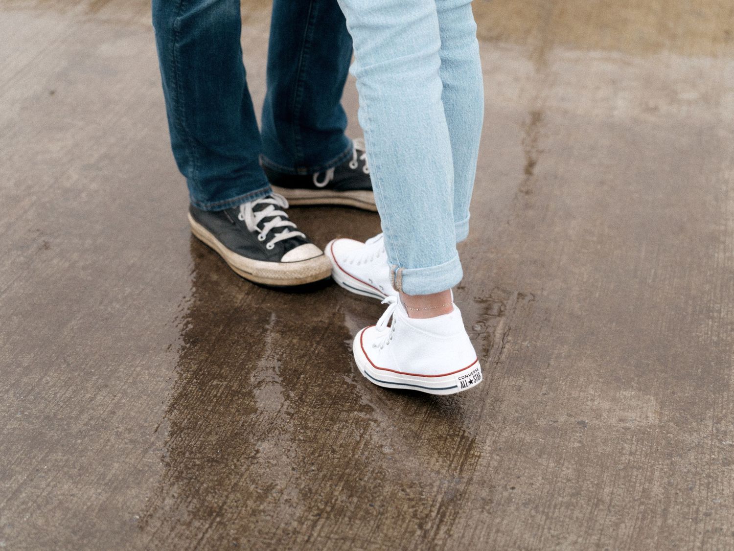 Two people wearing contrasting dark blue and white Converse sneakers standing close together on concrete ground.