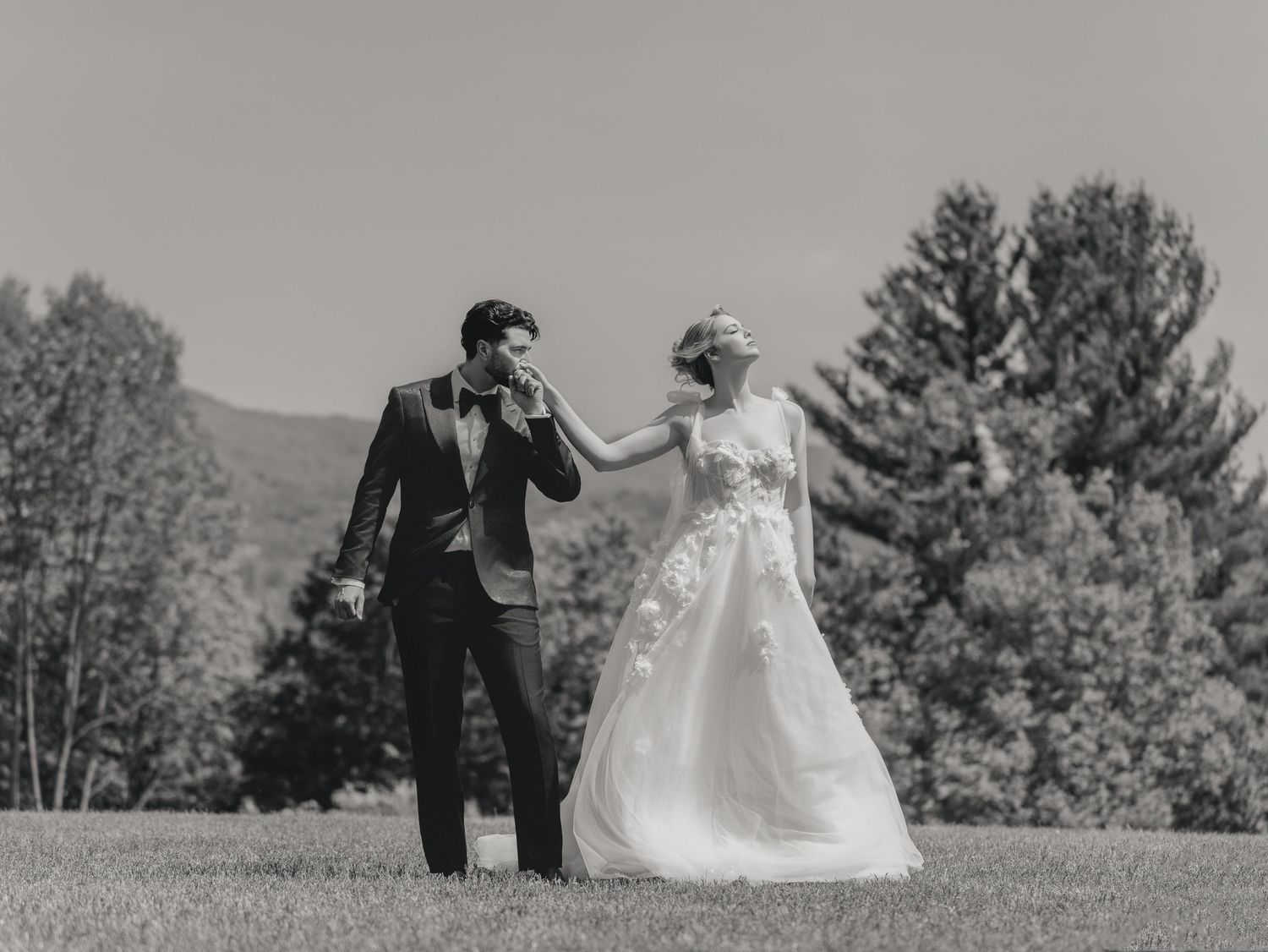 A joyful black and white wedding photo of newlyweds dancing in an outdoor setting.