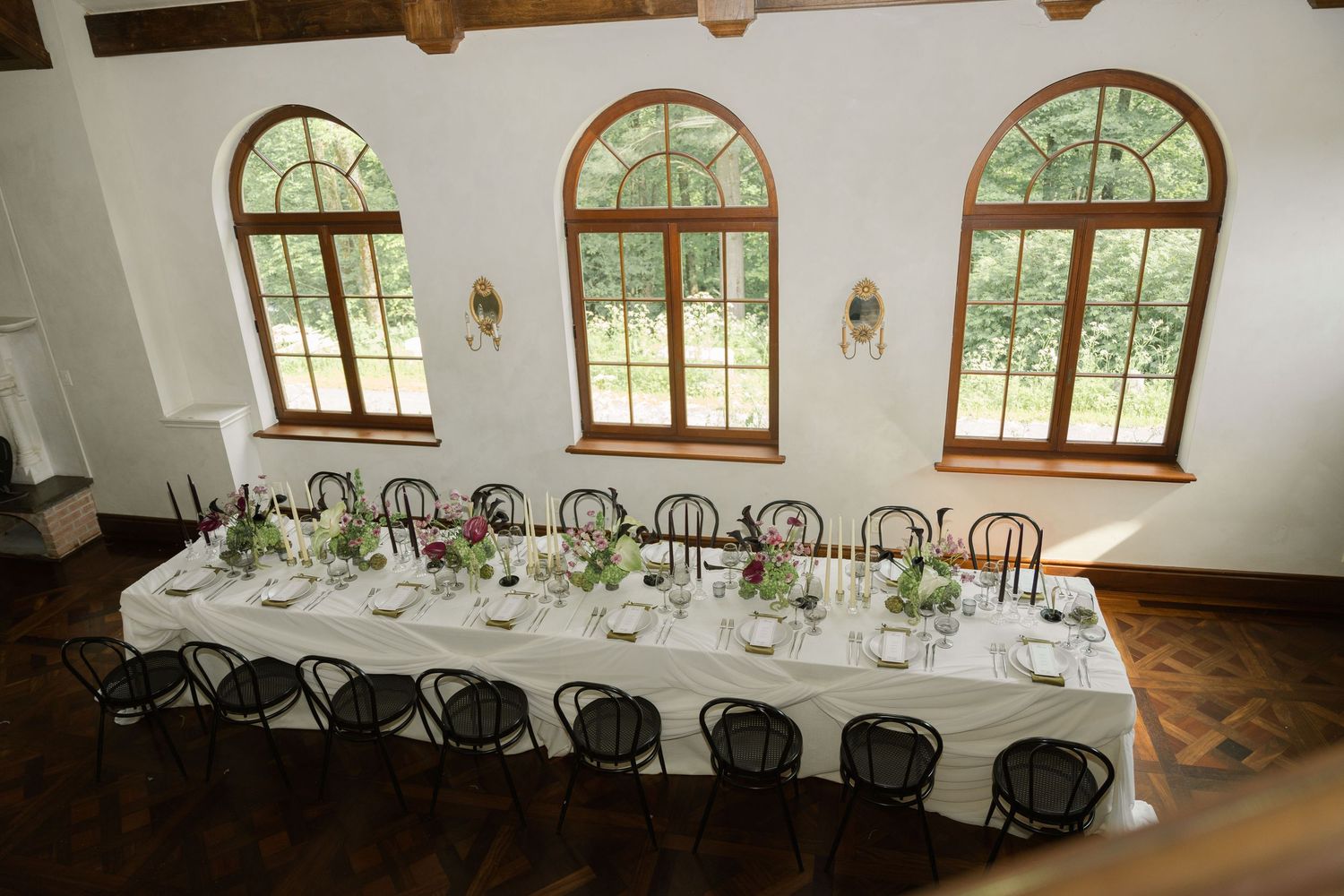 Long banquet tables set up in an elegant room with arched windows and wooden beams.